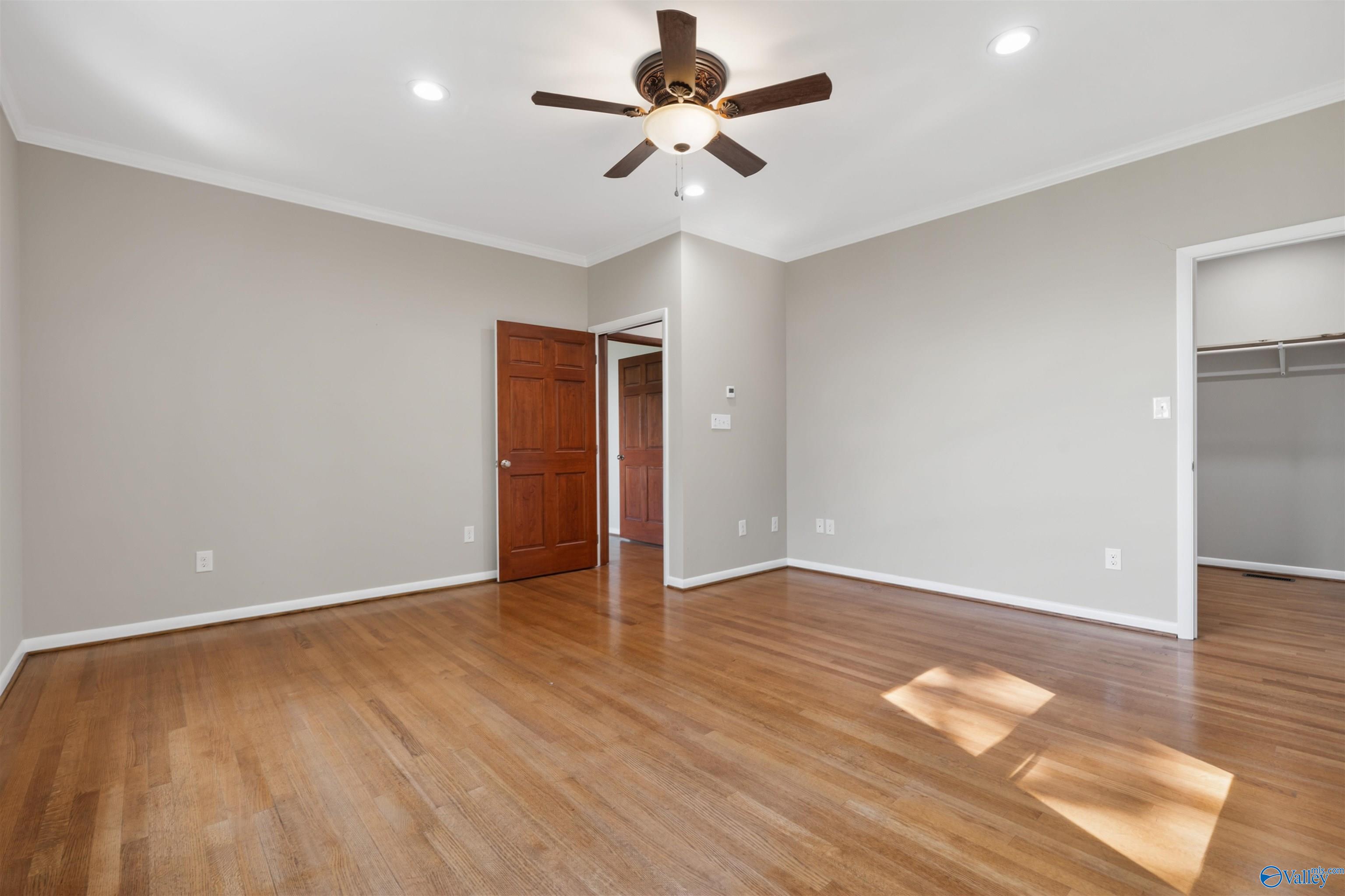 Empty bedroom with hardwood floors, a ceiling fan, and an open closet.