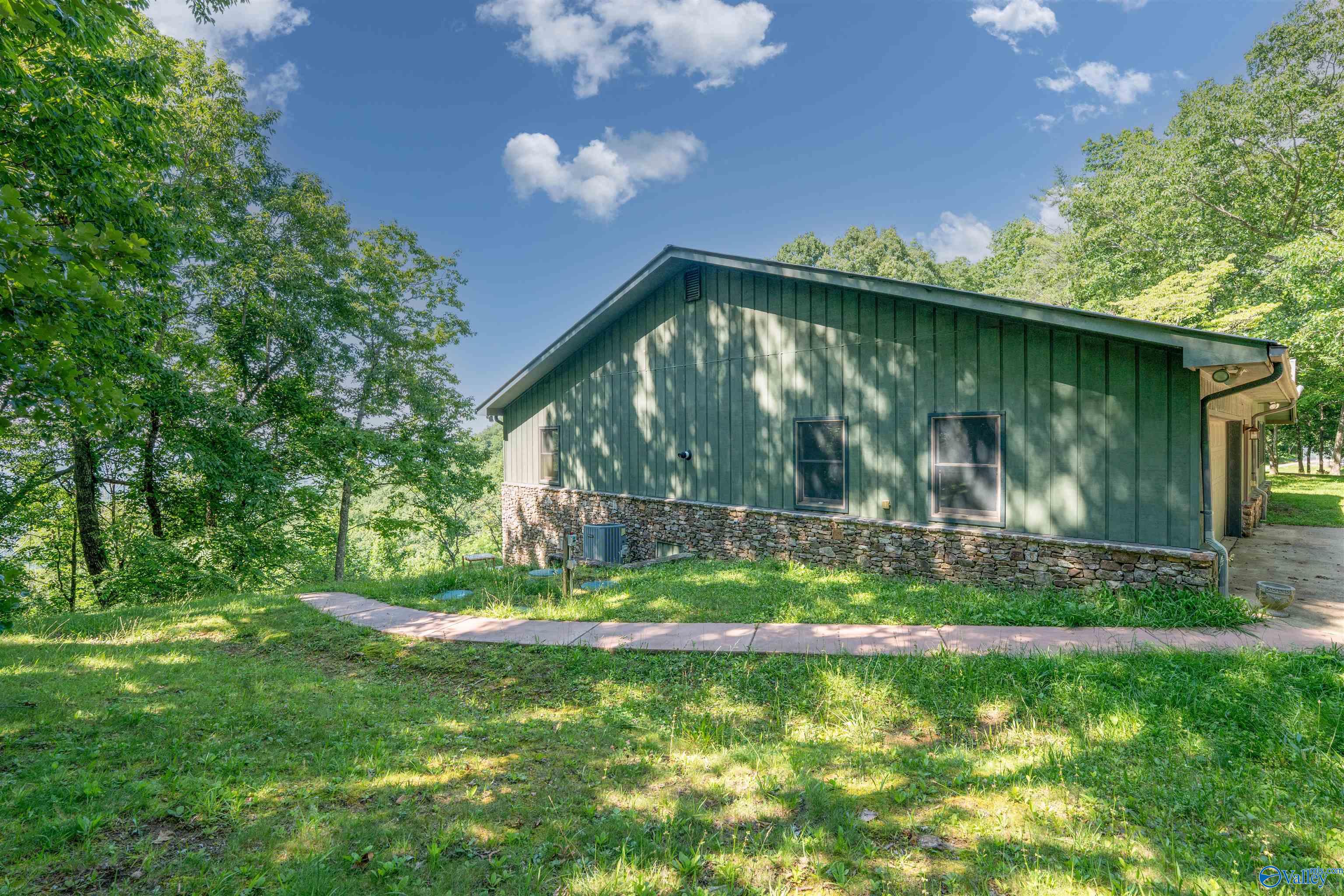 Green-sided home with a stone foundation and curved walkway in a leafy yard.