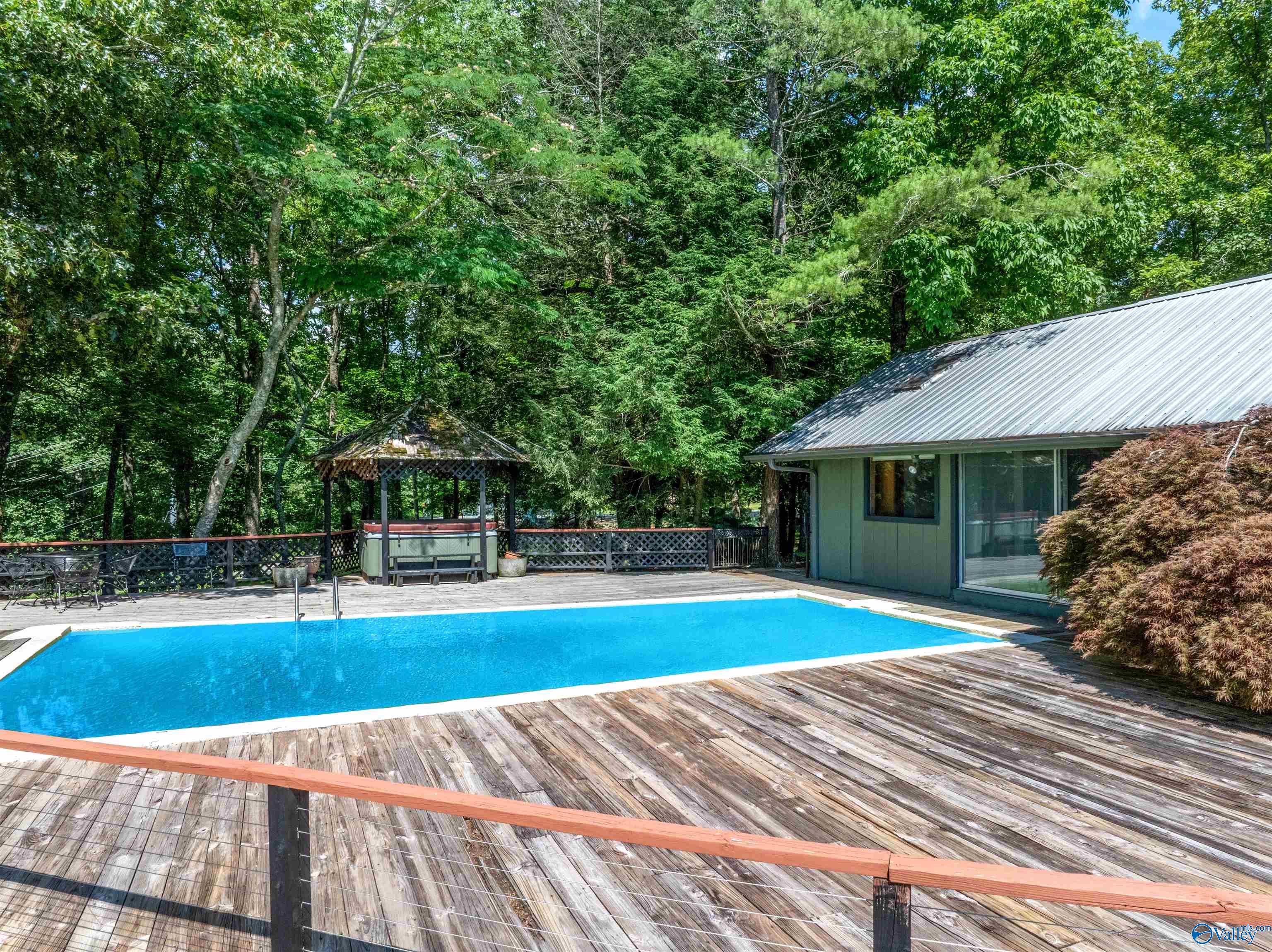Backyard pool with a large wooden deck and gazebo amid dense trees.