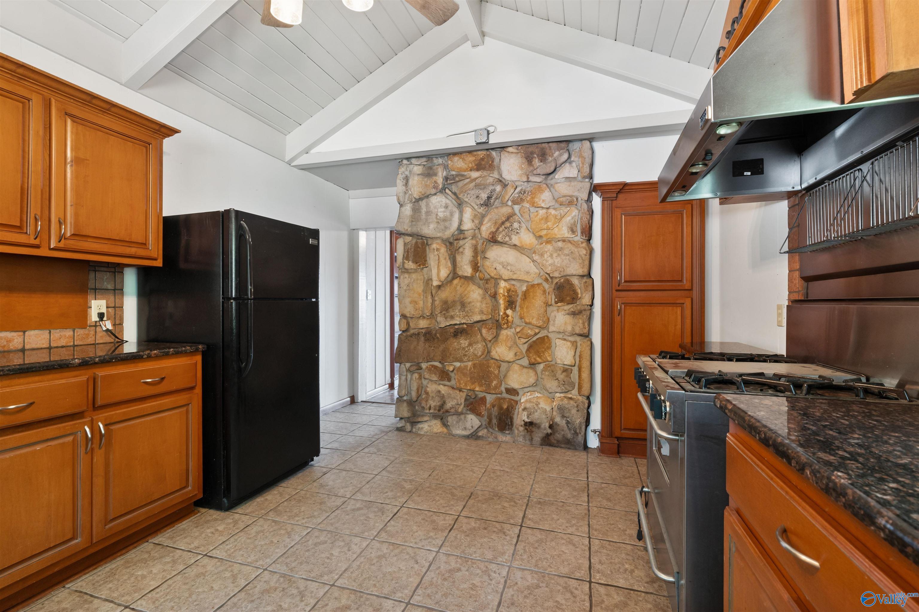 Kitchen with warm wood cabinets, a large stone partition, and a commercial-style range beneath a vaulted ceiling.