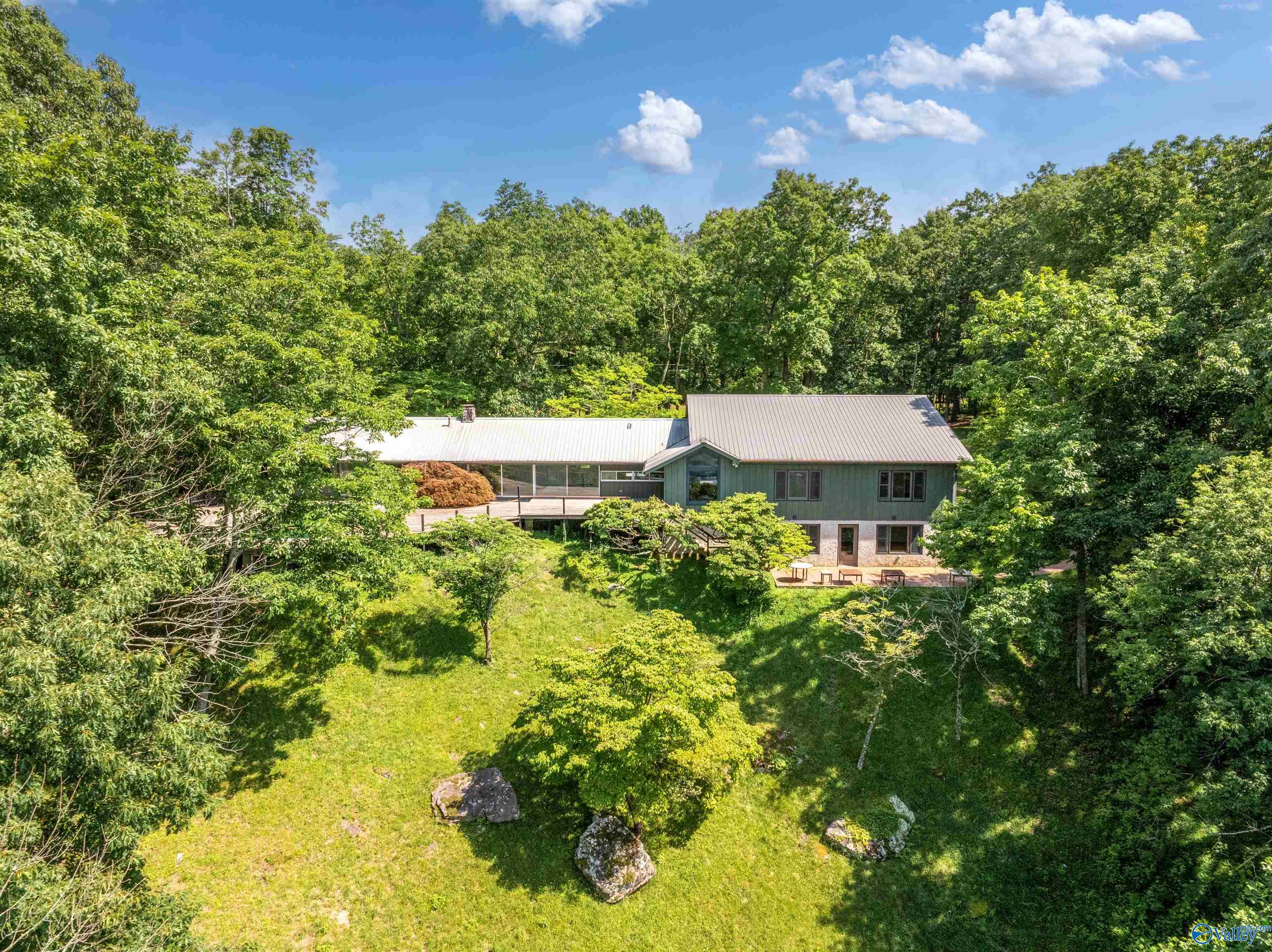 Aerial view of a green two-story home amid dense trees, with a metal roof and broad lawn.