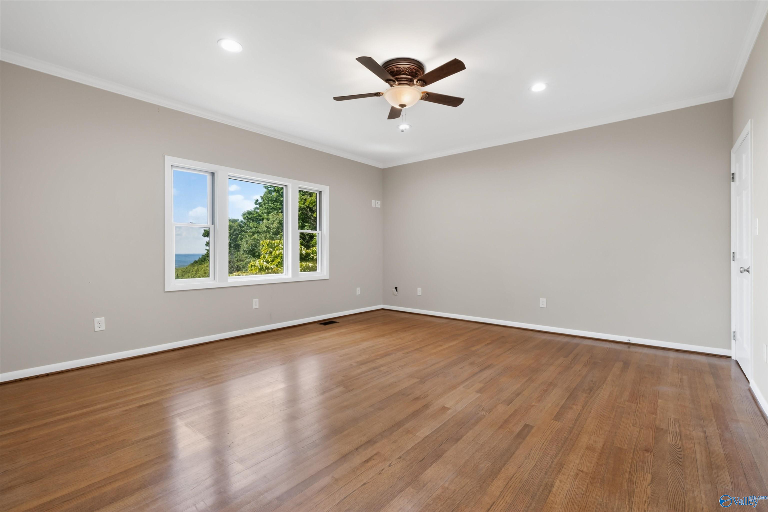 Empty bedroom with hardwood floors, a ceiling fan, and a window overlooking greenery and water.
