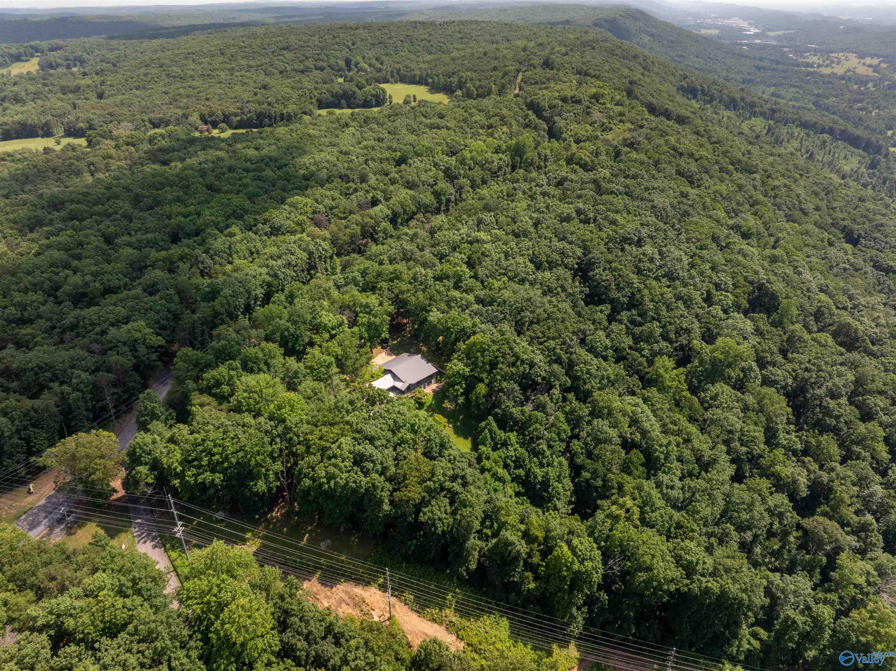 Aerial view of a house tucked among dense woods, with distant ridgelines beyond.