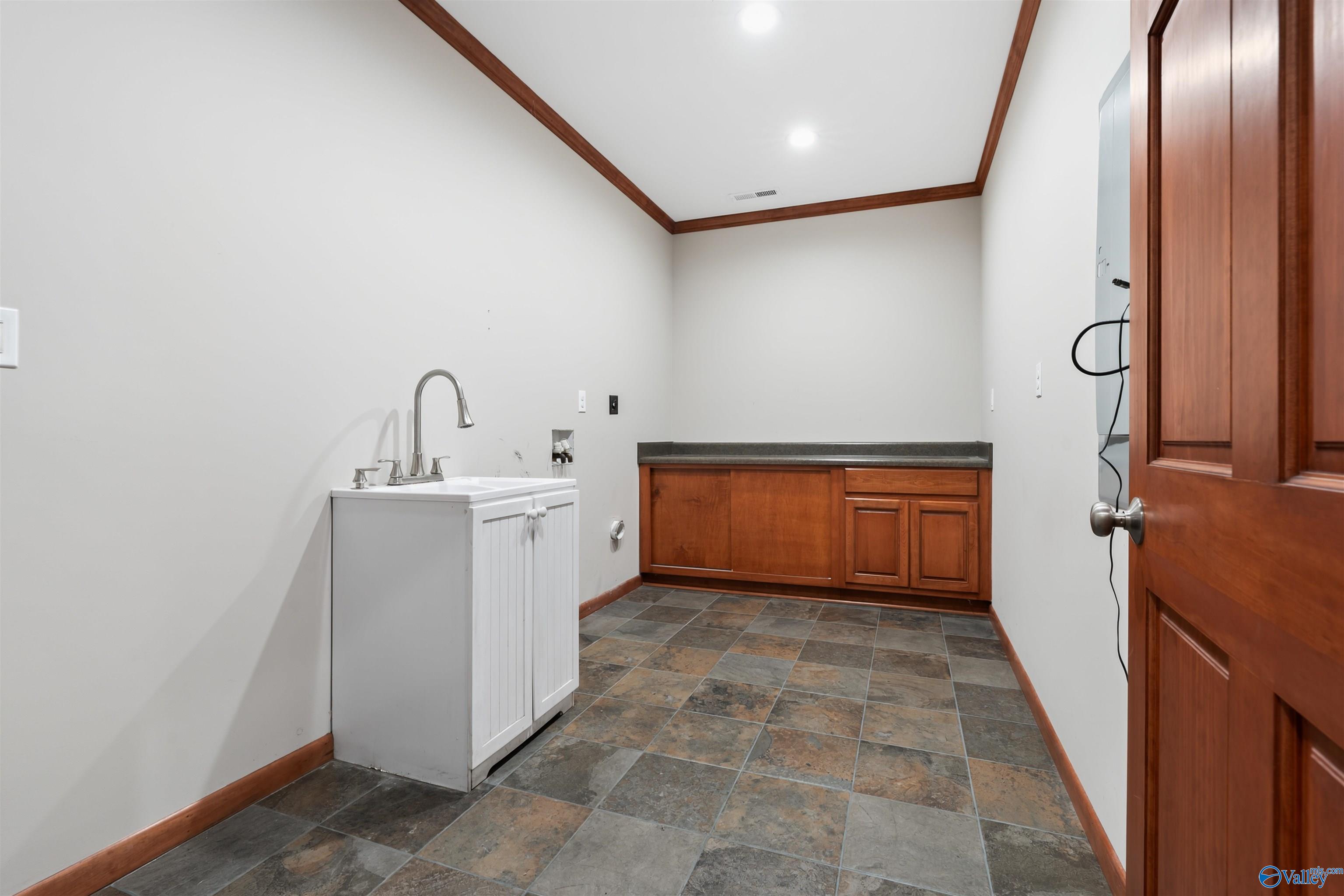 Laundry room with a utility sink, wood cabinets, stone-pattern tile floor, and visible washer hookups.