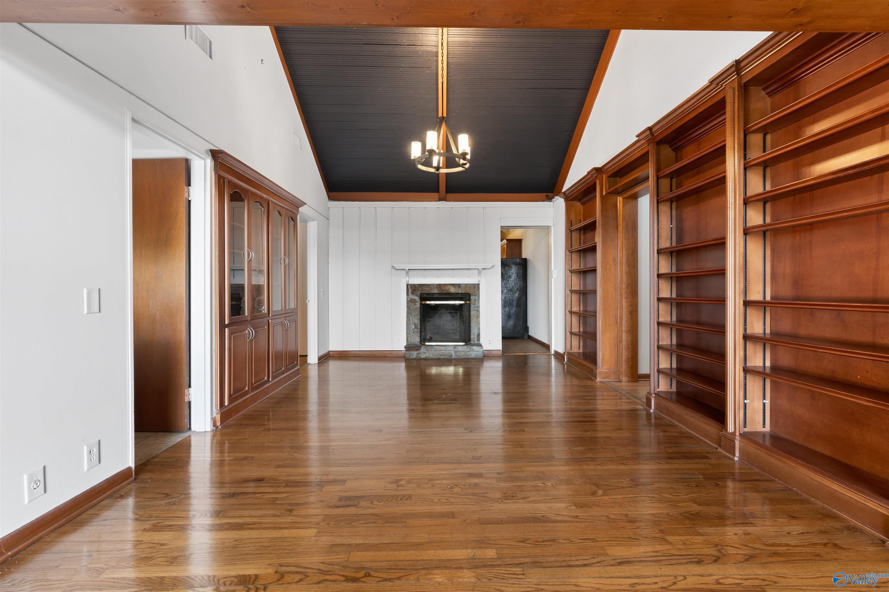 Empty room with built-in wooden bookshelves, hardwood floors, and a stone fireplace.