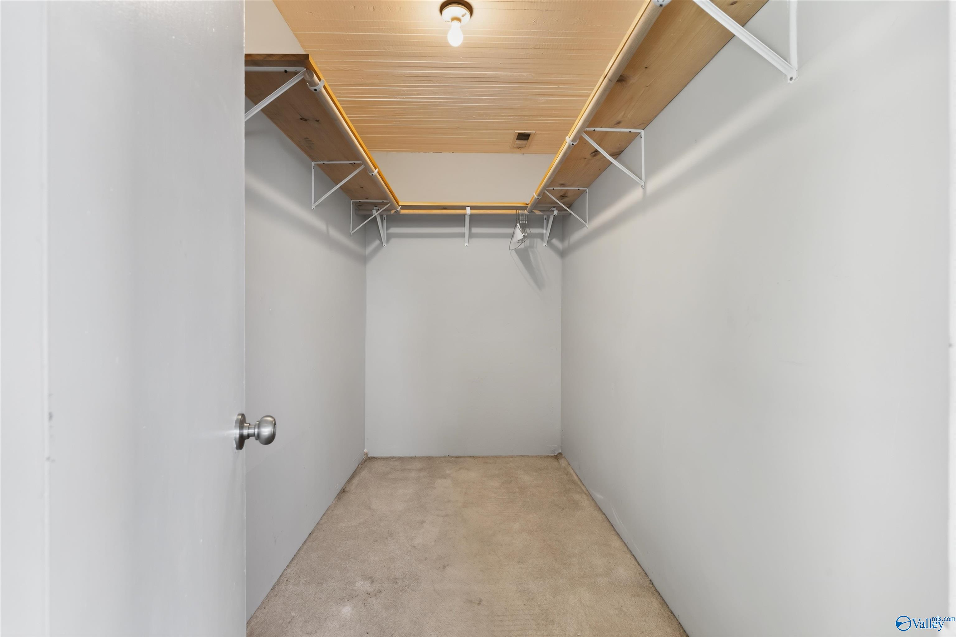 Empty walk-in closet with high wooden shelves and beige carpet.