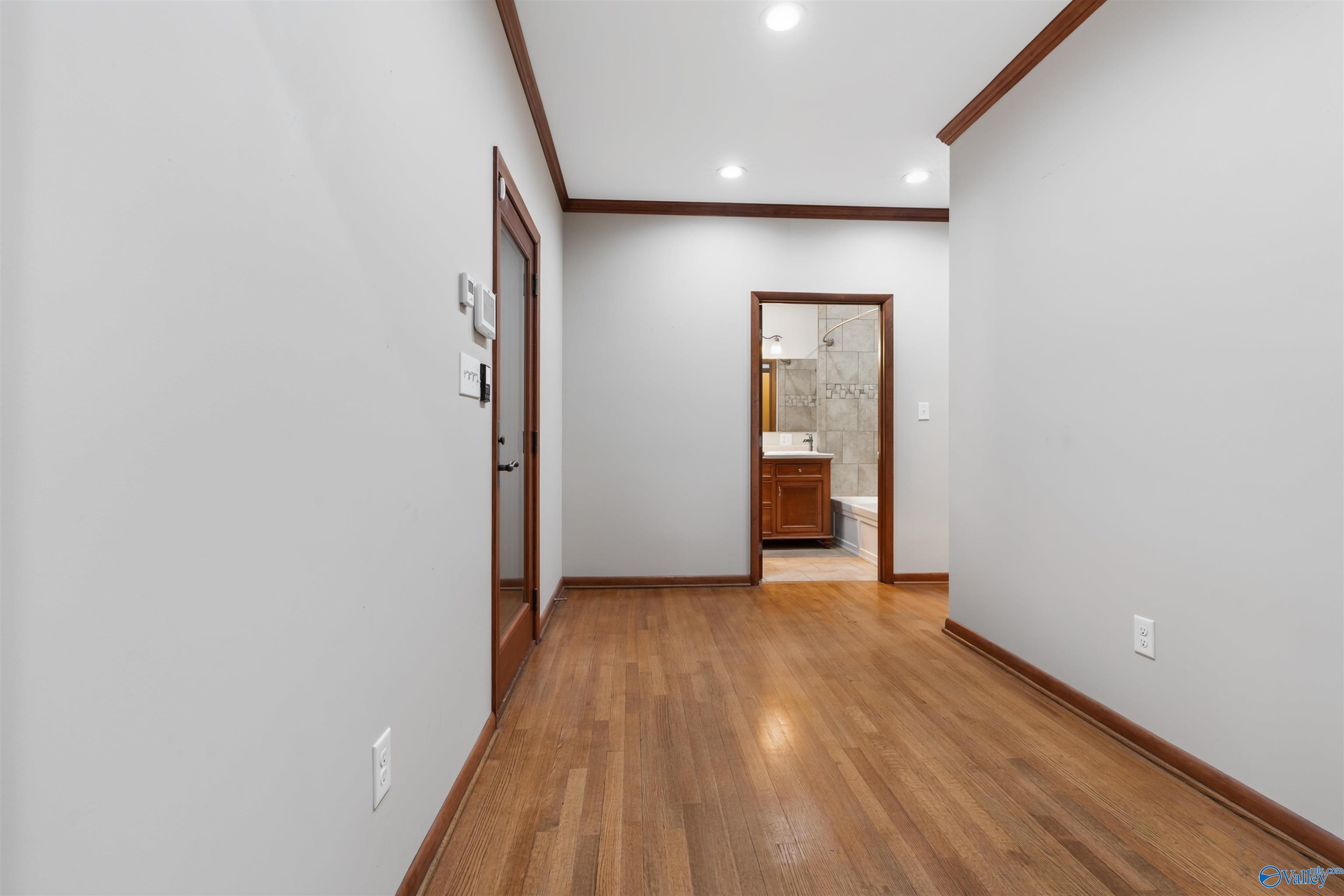 Hallway with hardwood floors and dark wood trim, opening onto a bathroom.