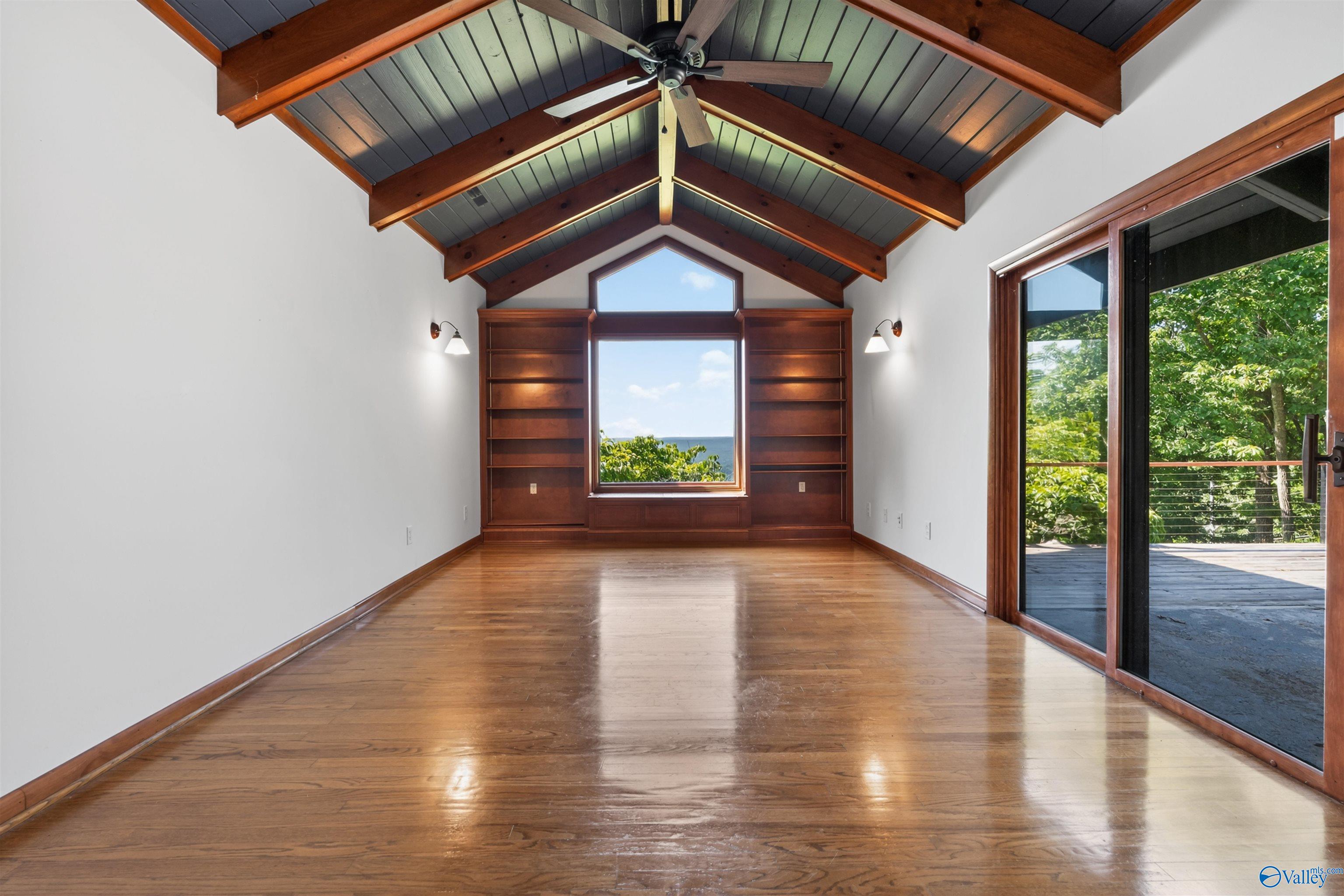 Empty room with vaulted timber ceiling, built-in shelves, and sliding doors to a leafy deck.