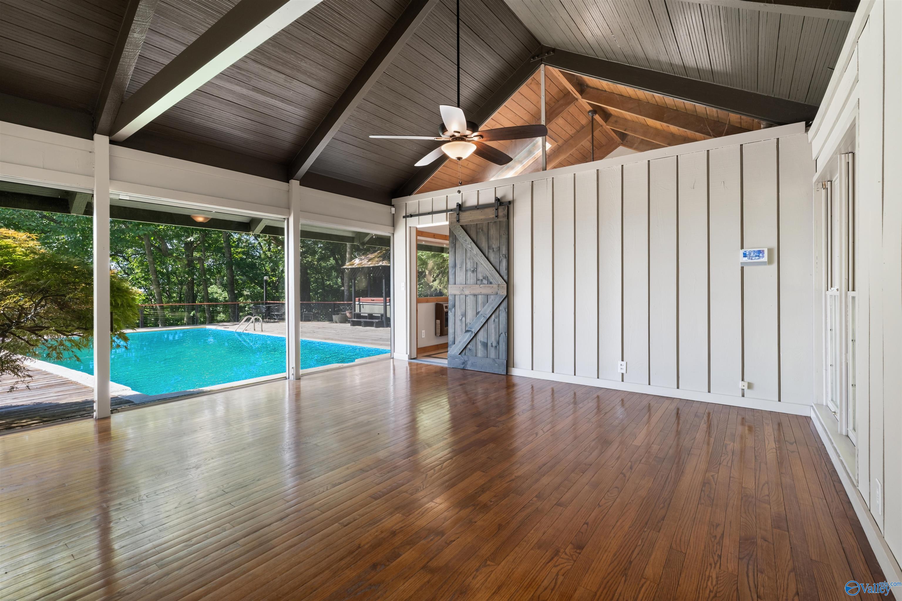 Empty hardwood-floored room with a vaulted wood ceiling and open views of a swimming pool.