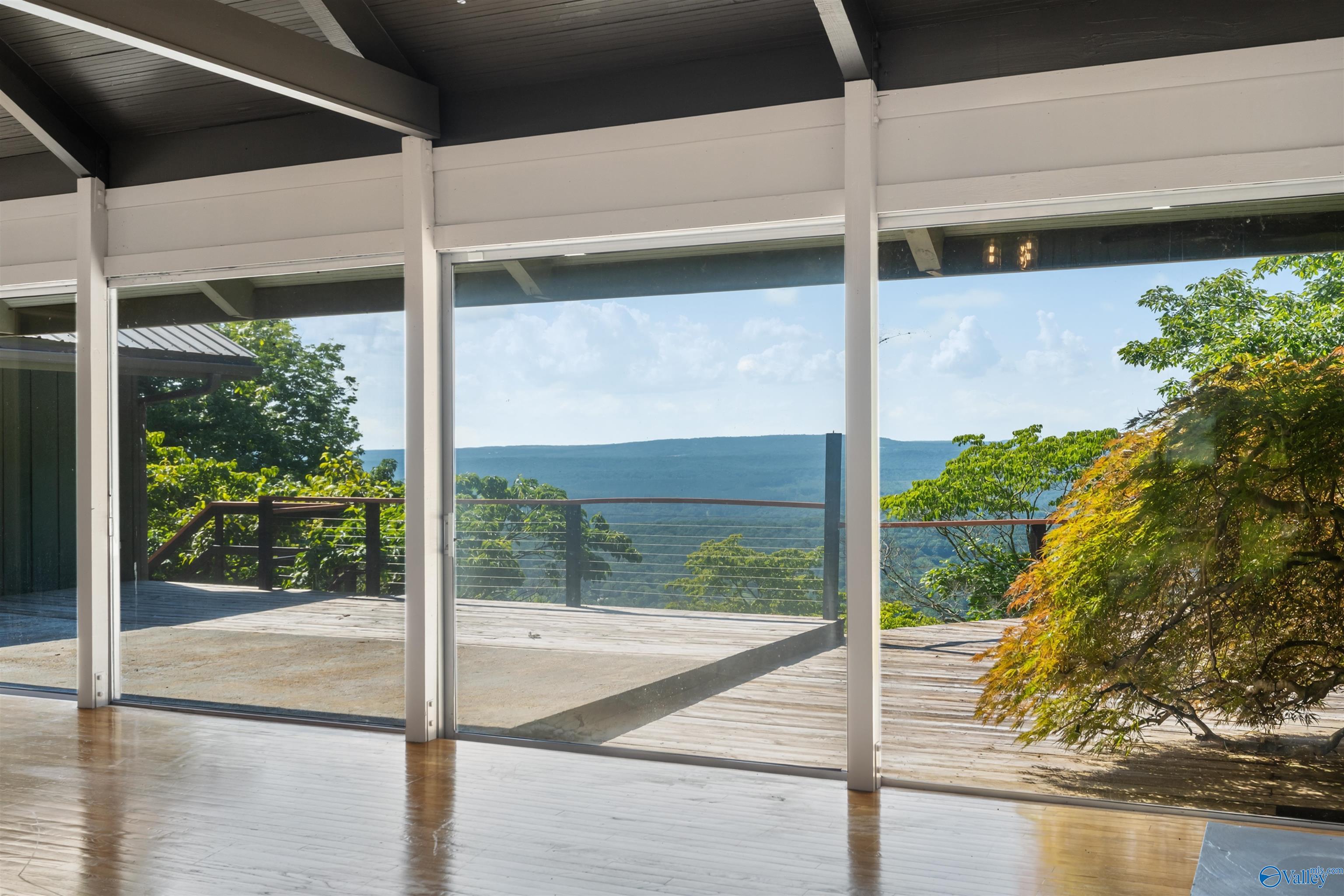 Empty room with floor-to-ceiling windows overlooking a wooden deck and distant mountain ridges.