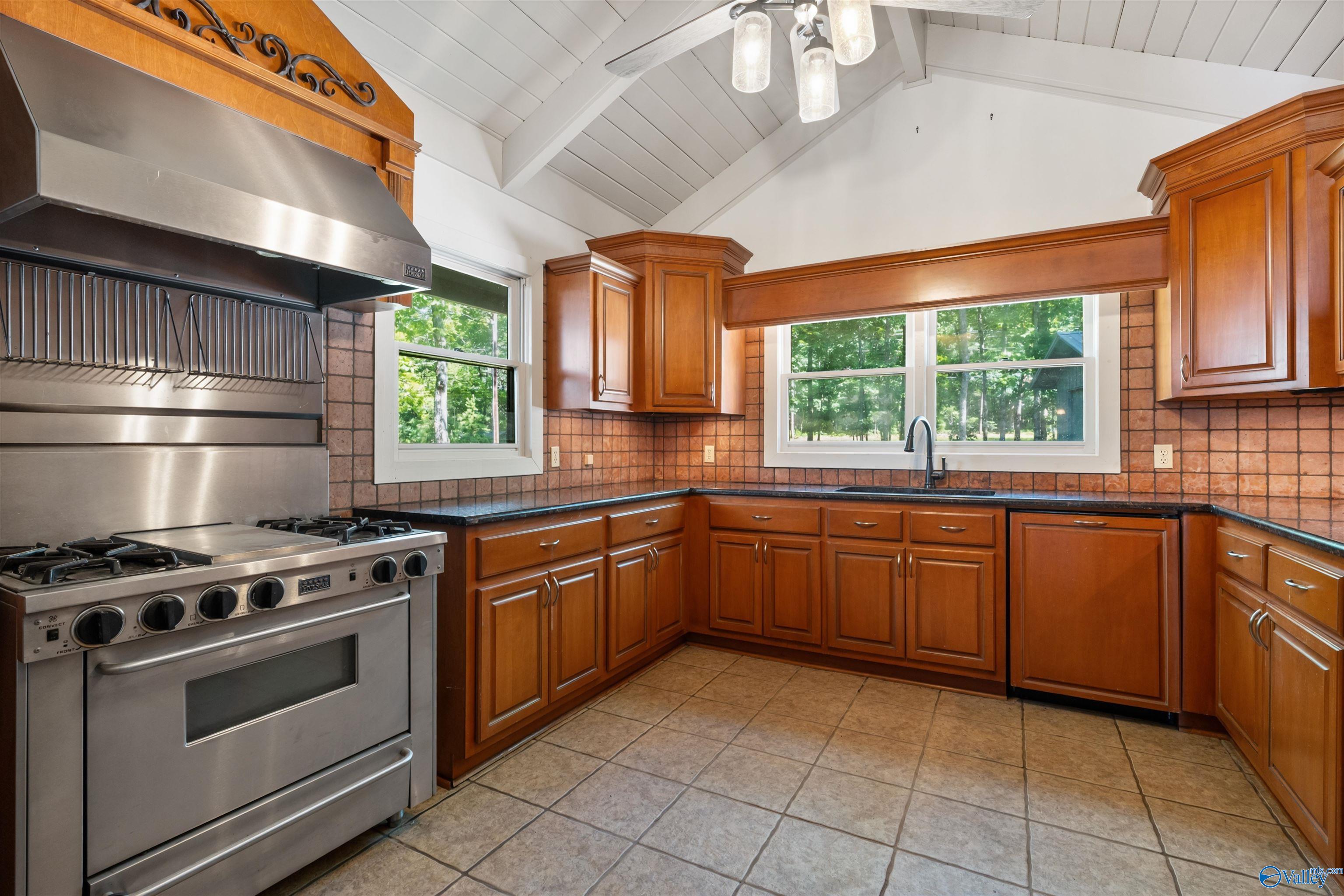 Kitchen with warm wood cabinets, stainless steel range, tile backsplash, and windows overlooking trees.