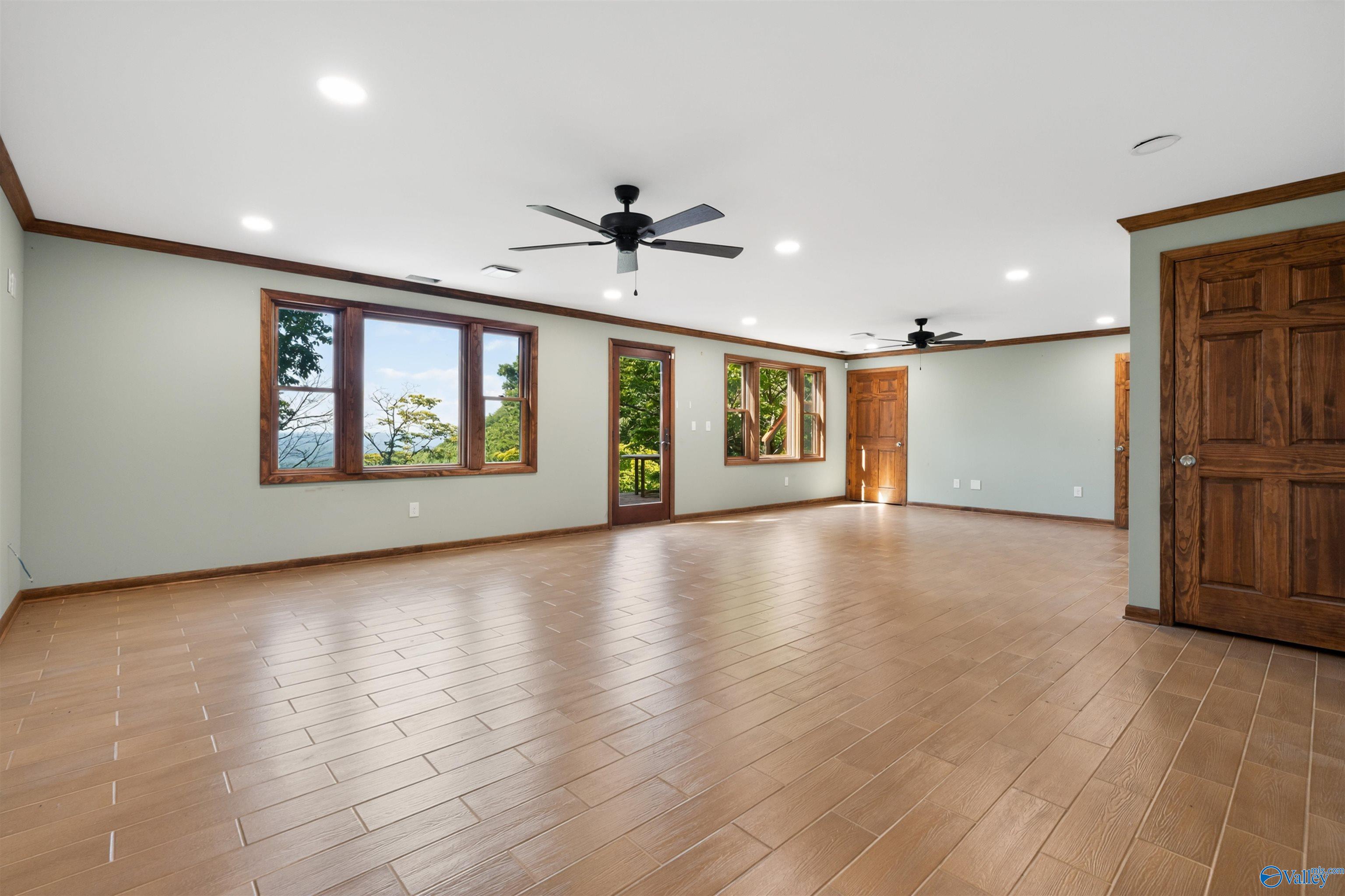 Vacant room with tan tile flooring, dark wood trim, ceiling fans, and windows overlooking trees and distant ridges.