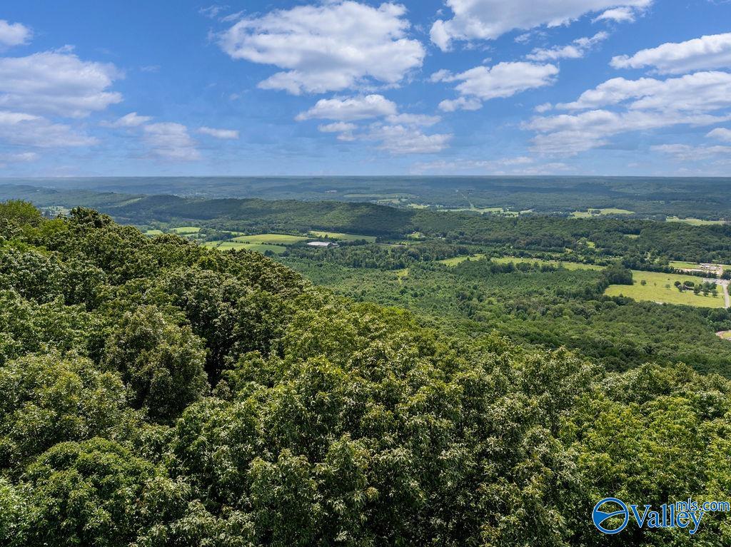 Wooded hills and green fields stretch across a broad valley beneath a blue, cloud-filled sky.