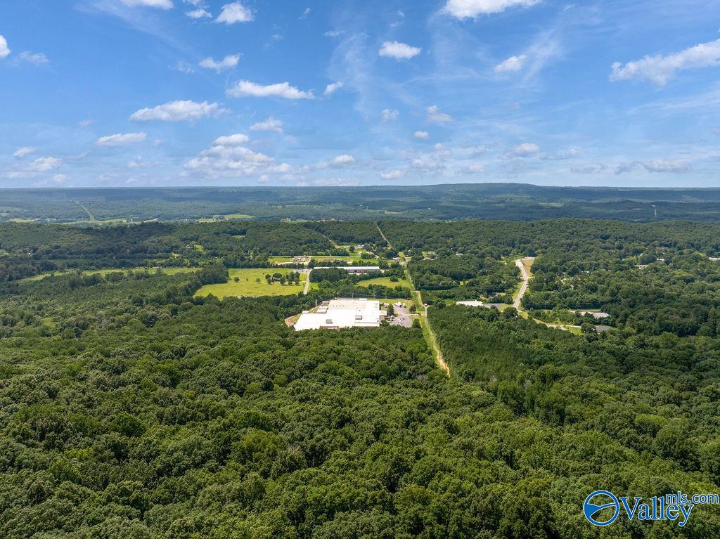 Aerial view of wooded acreage with a clearing, roads, and distant buildings.