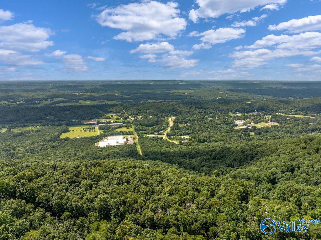 Aerial view of wooded countryside, fields, and scattered buildings beneath a cloud-filled sky.