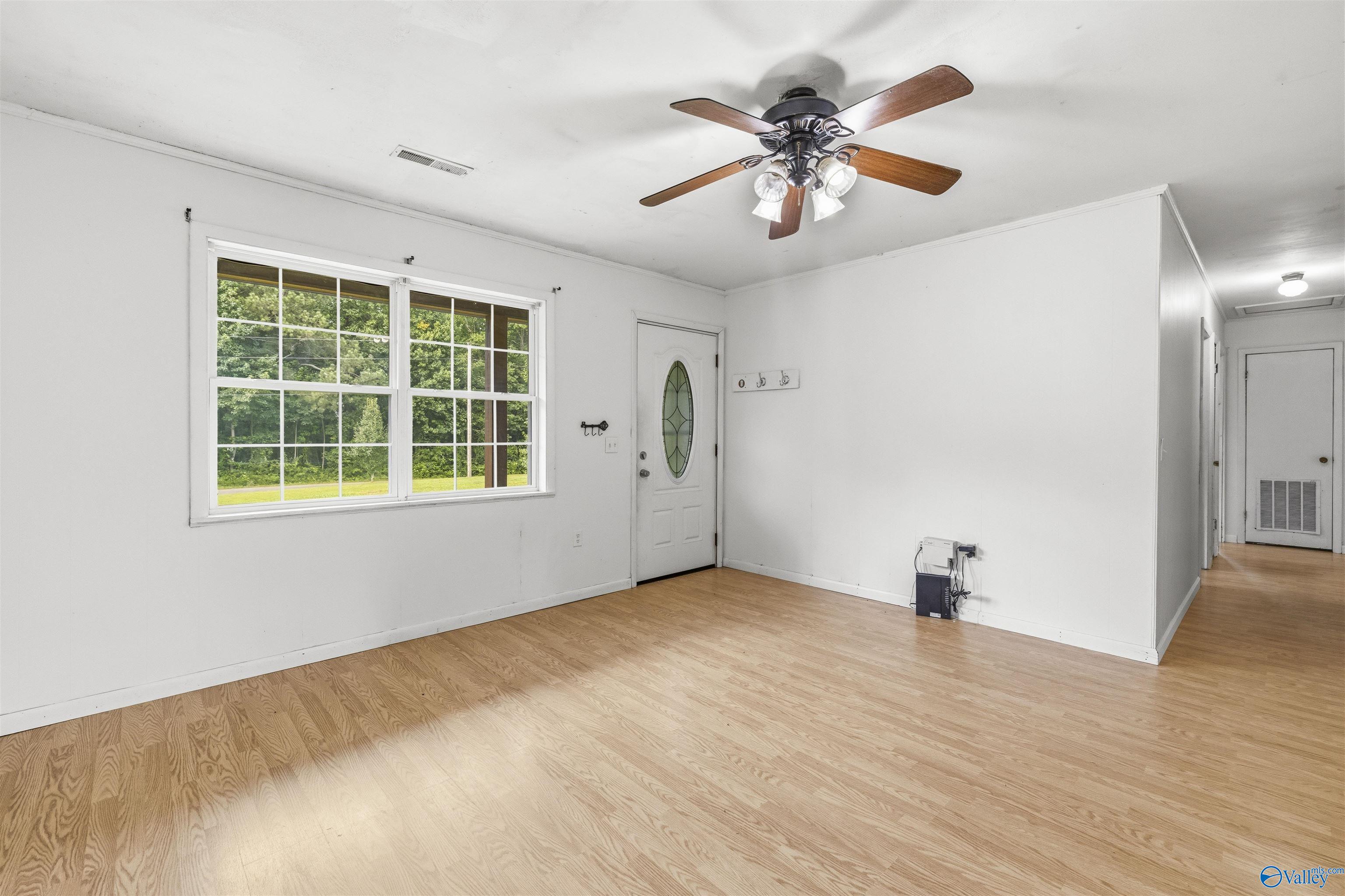 Empty room with light wood flooring, large windows overlooking trees, and a ceiling fan.