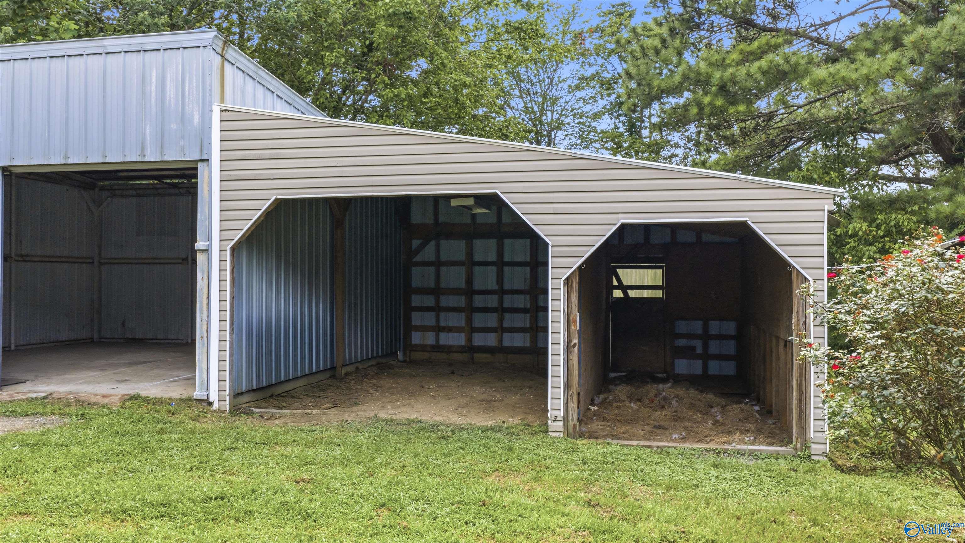 Barn with three open bays and two animal stalls beside a grassy yard.