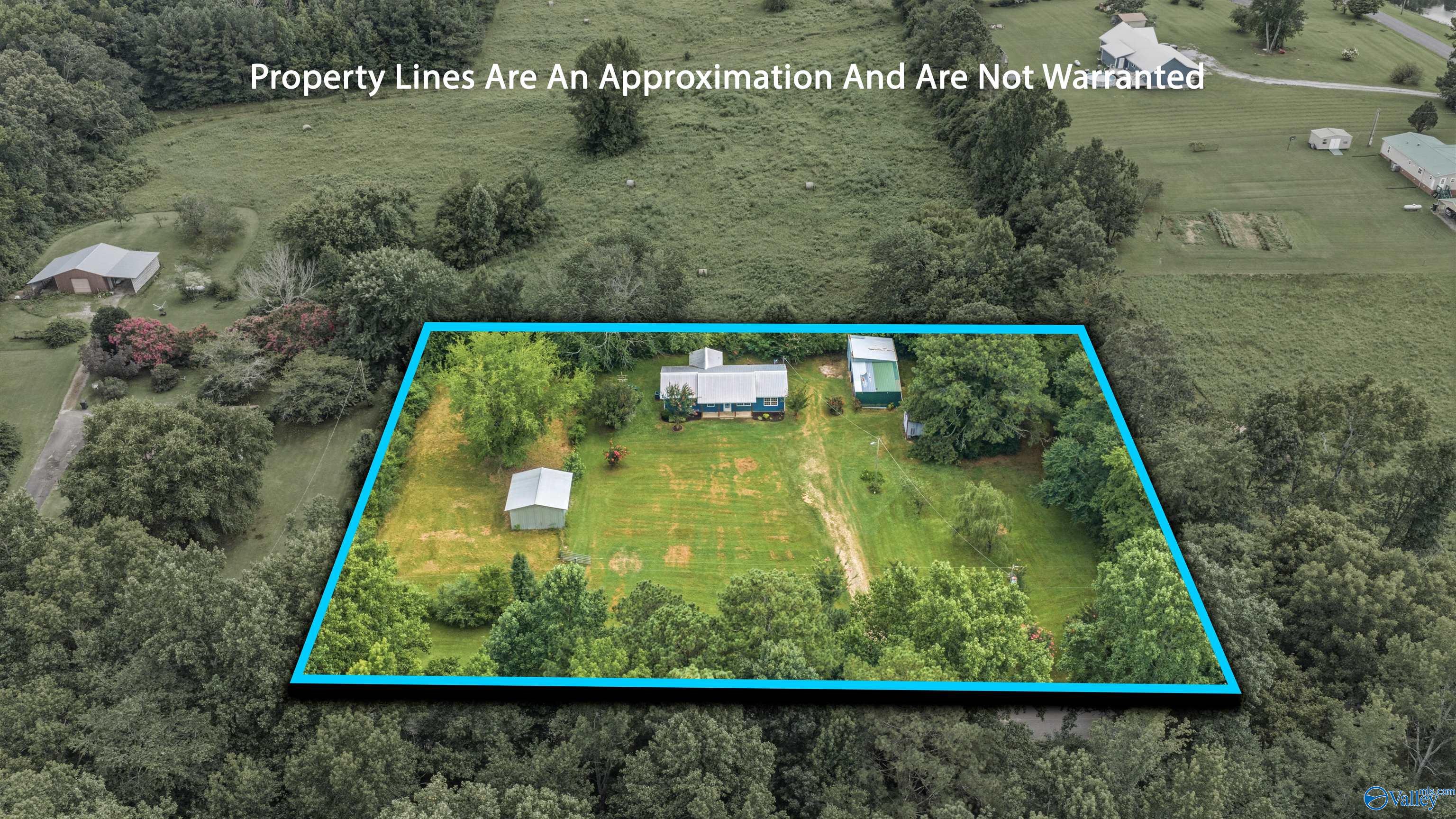 Aerial view of a rural home and outbuildings within a blue-outlined, tree-lined property.
