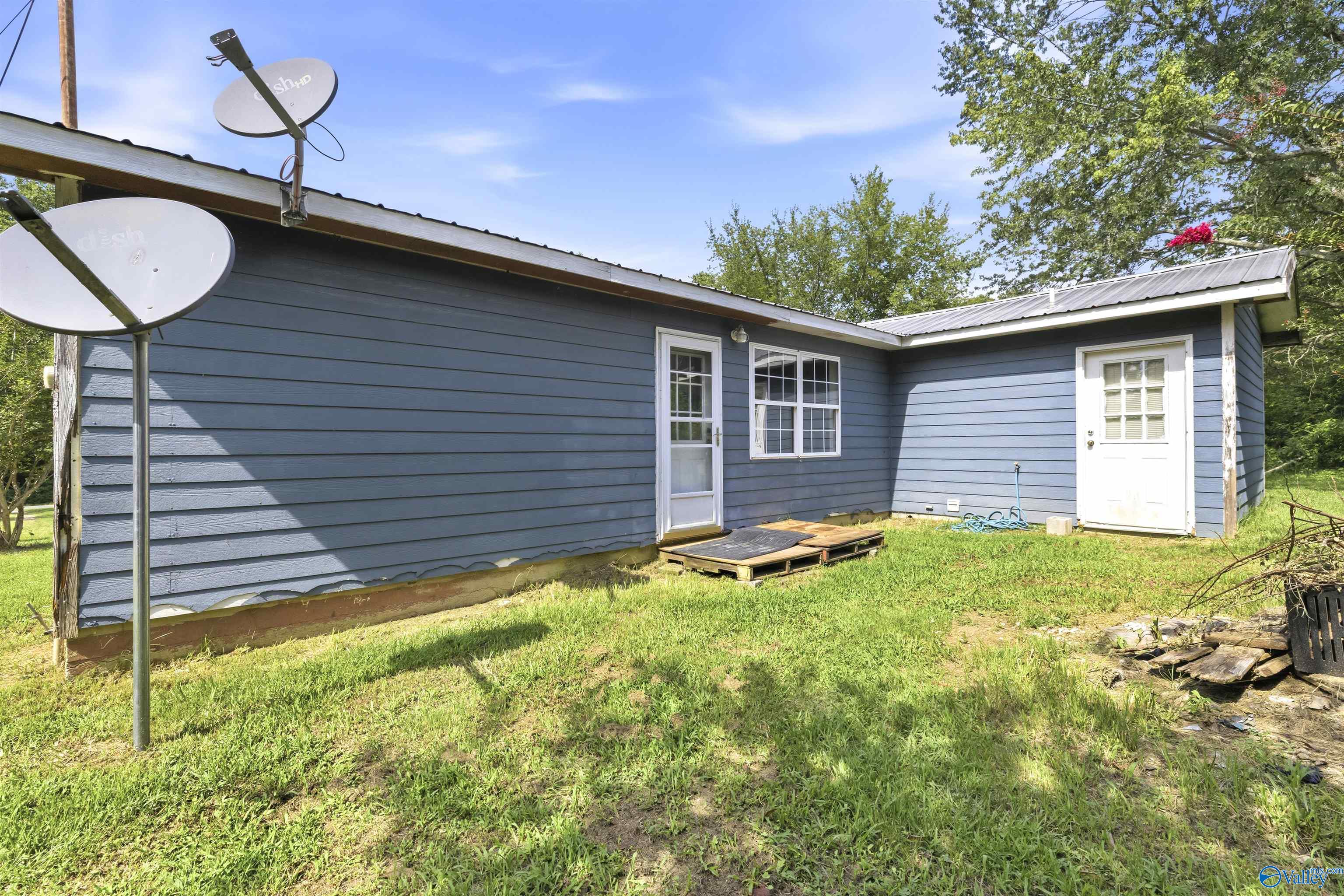 Blue-sided home exterior with two white doors, satellite dishes, and a grassy yard.