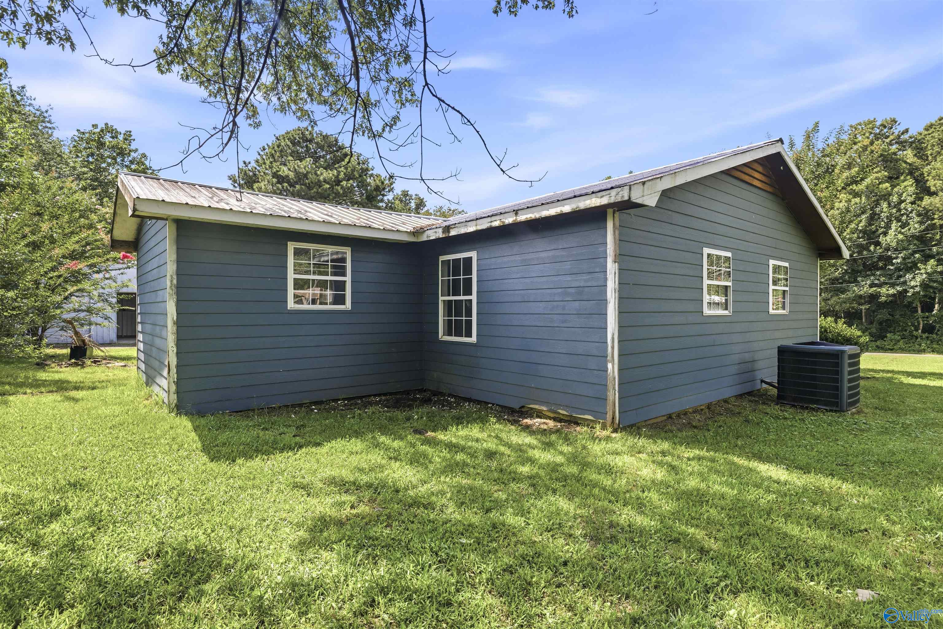 Blue single-story house with white-trimmed windows, a metal roof, and a grassy yard.
