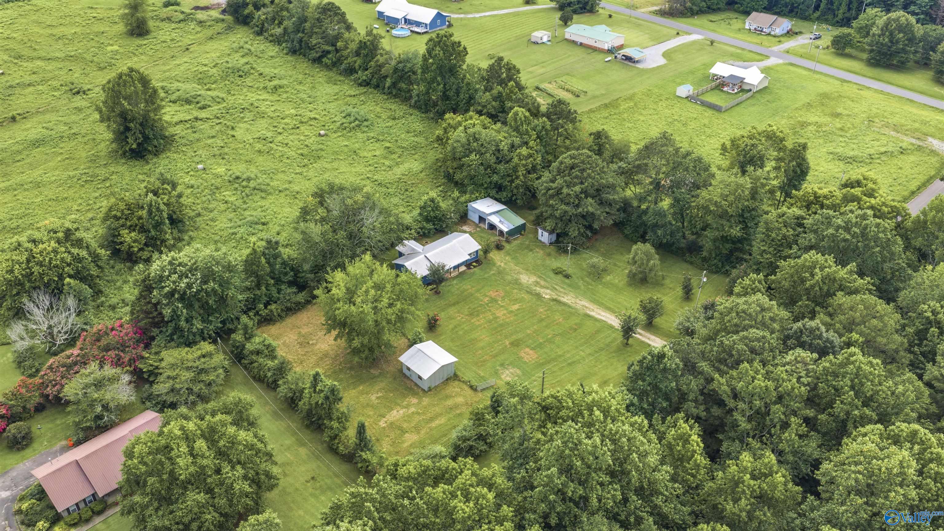 Aerial view of a rural home with a broad lawn, outbuildings, and surrounding trees.