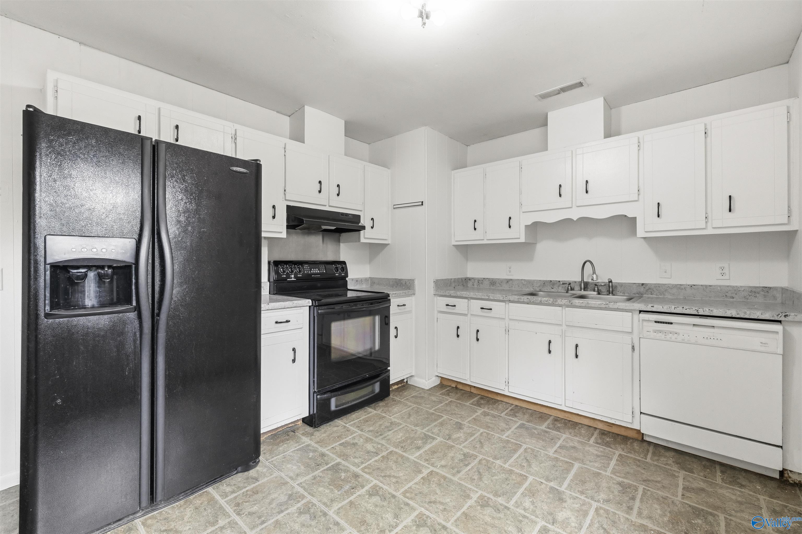 Kitchen with white cabinets, gray tile floors, and black refrigerator and range.