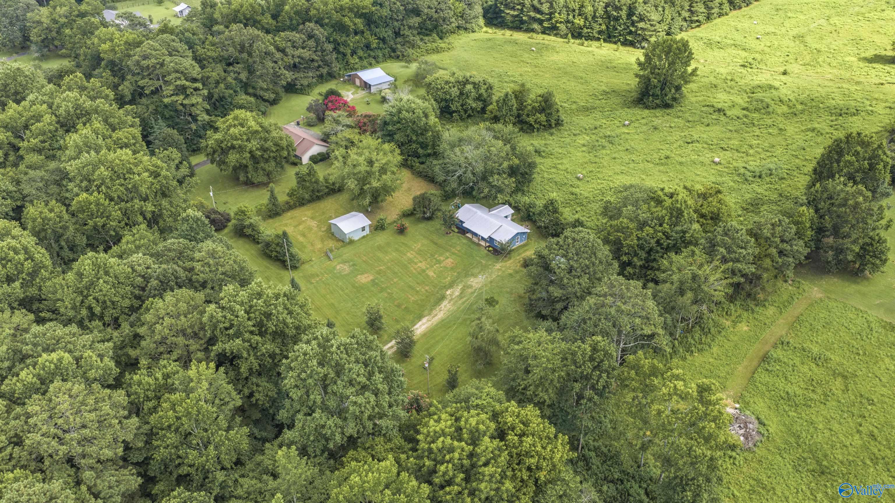 Aerial view of a rural home and outbuildings surrounded by pasture and trees.