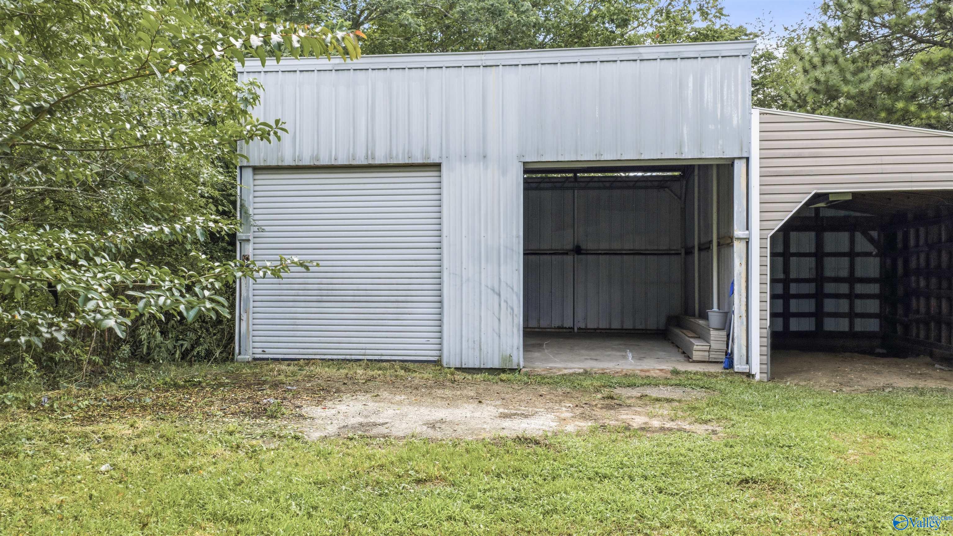 Detached white metal garage with a closed roll-up door and open bay beside a beige open-sided garage.