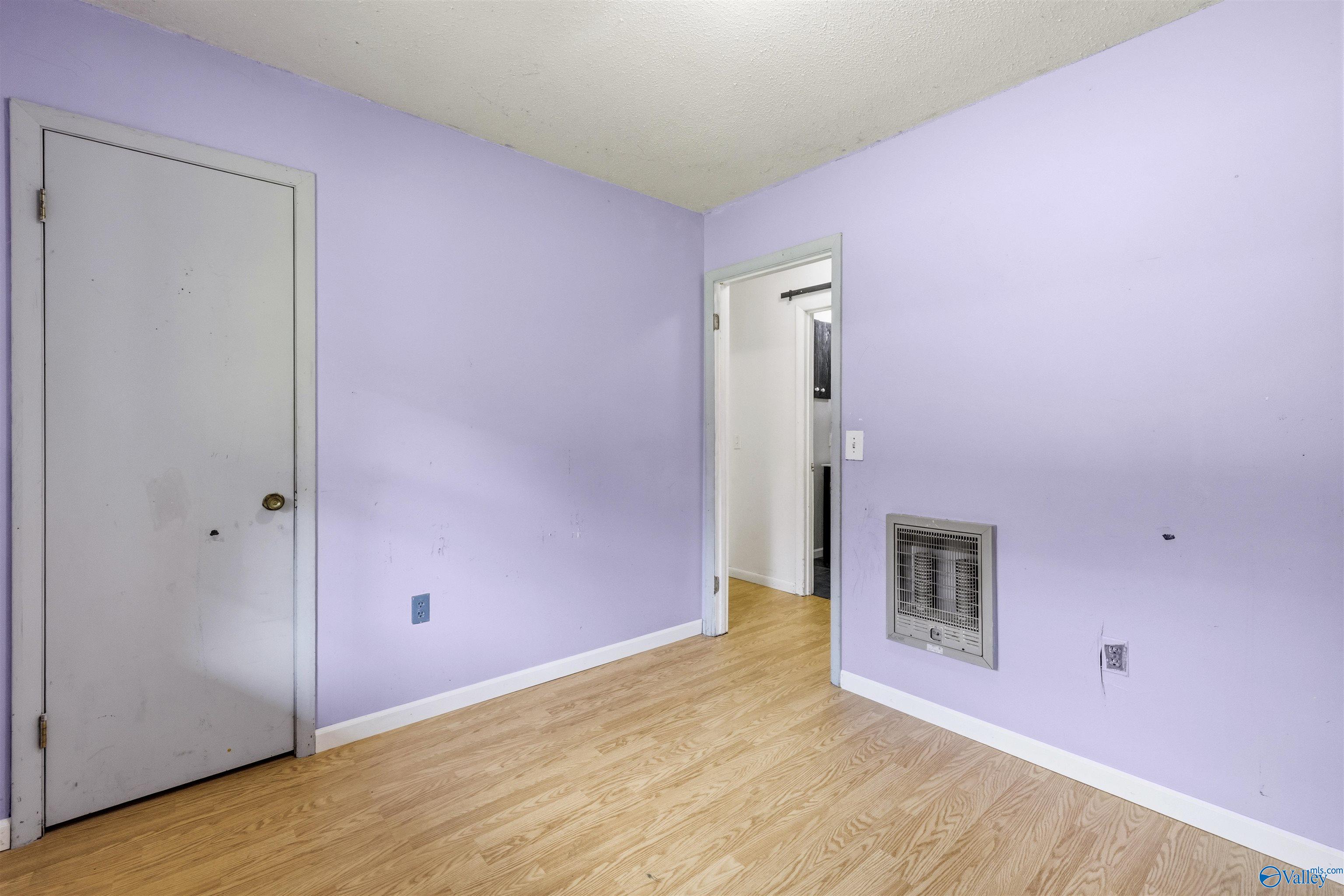 Empty room with pale purple walls, light wood flooring, and a wall-mounted heater.
