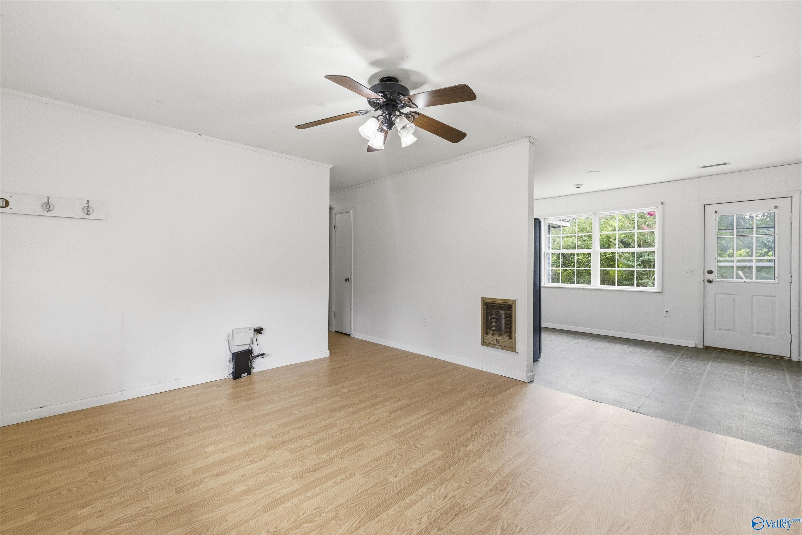 Vacant living room with wood flooring, ceiling fan, and adjoining tiled entry area.
