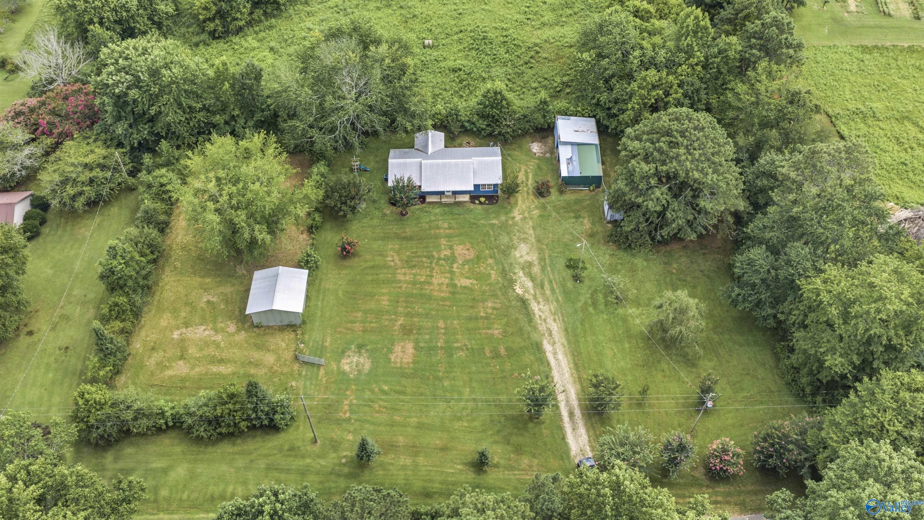 Aerial view of a home and two outbuildings in a wooded rural yard.