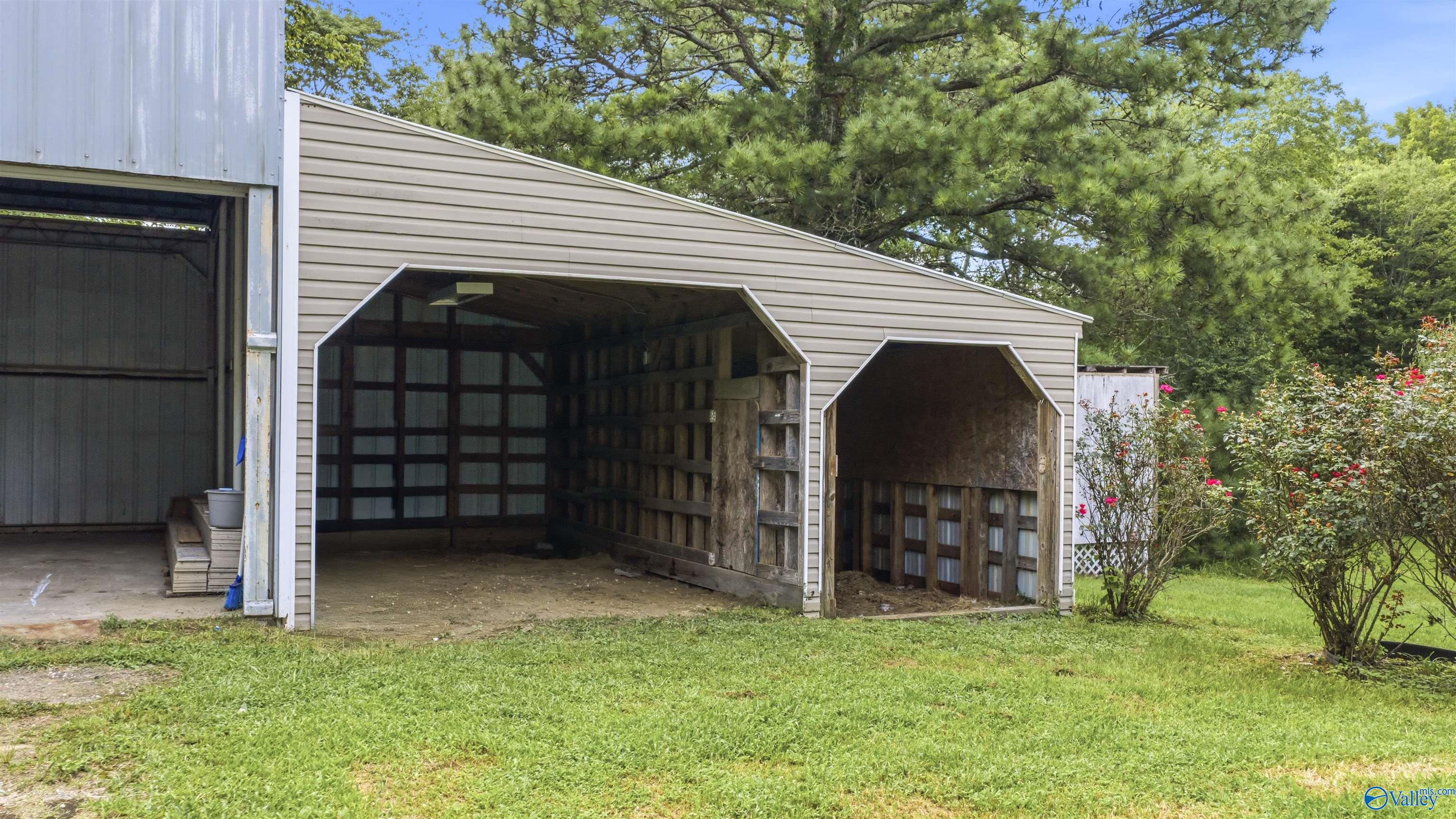 Open-front storage sheds with exposed timber framing beside a grassy yard and flowering shrubs.