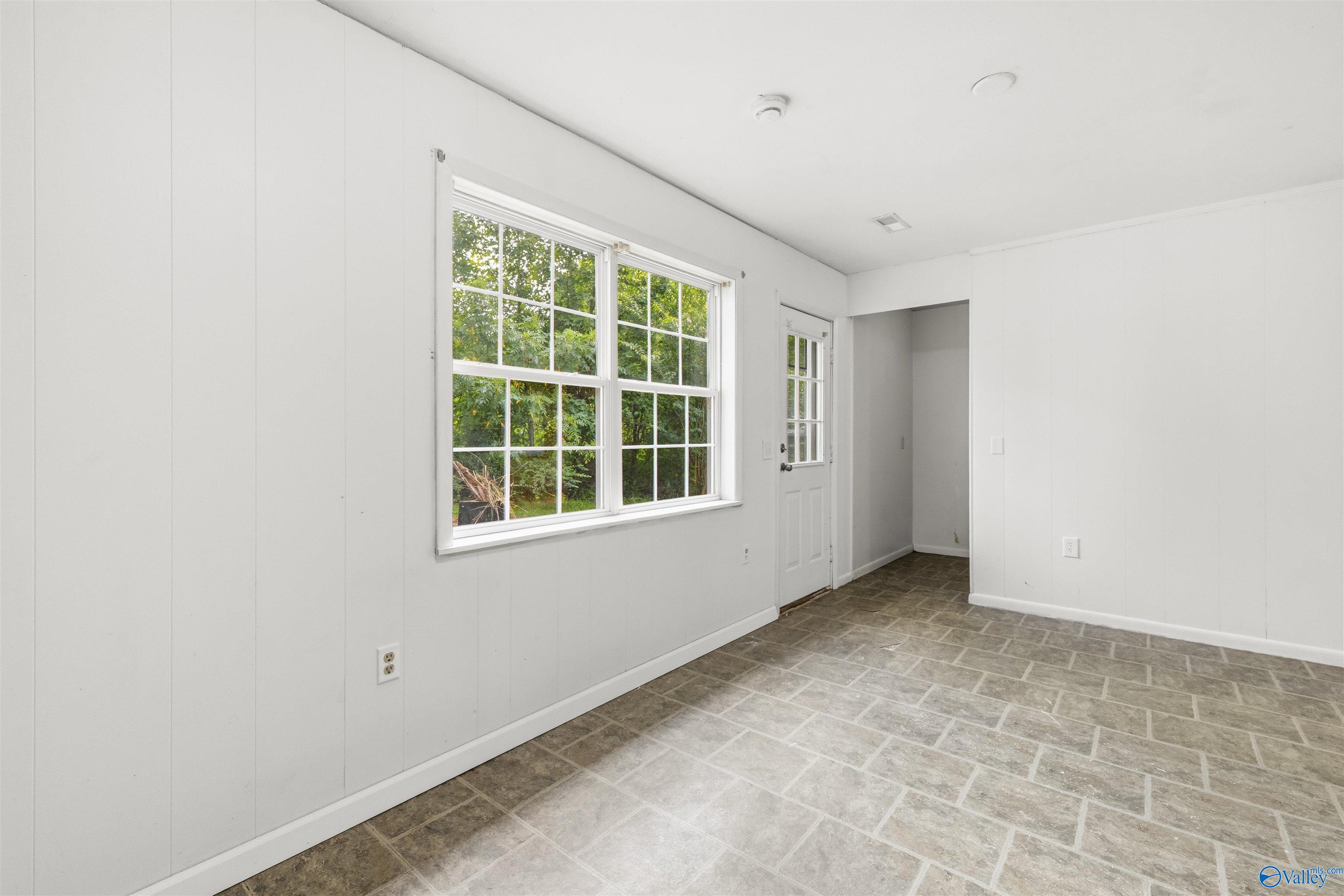 Vacant room with a tiled floor, large divided-light windows, and a glass-paneled exterior door.