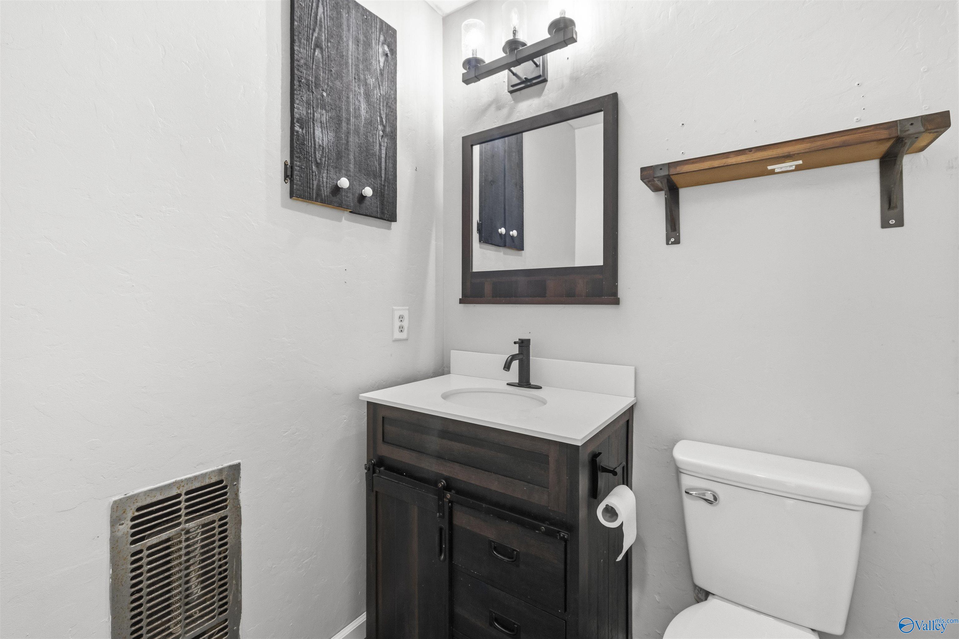 Bathroom with a dark wood vanity, white sink, framed mirror, and toilet.