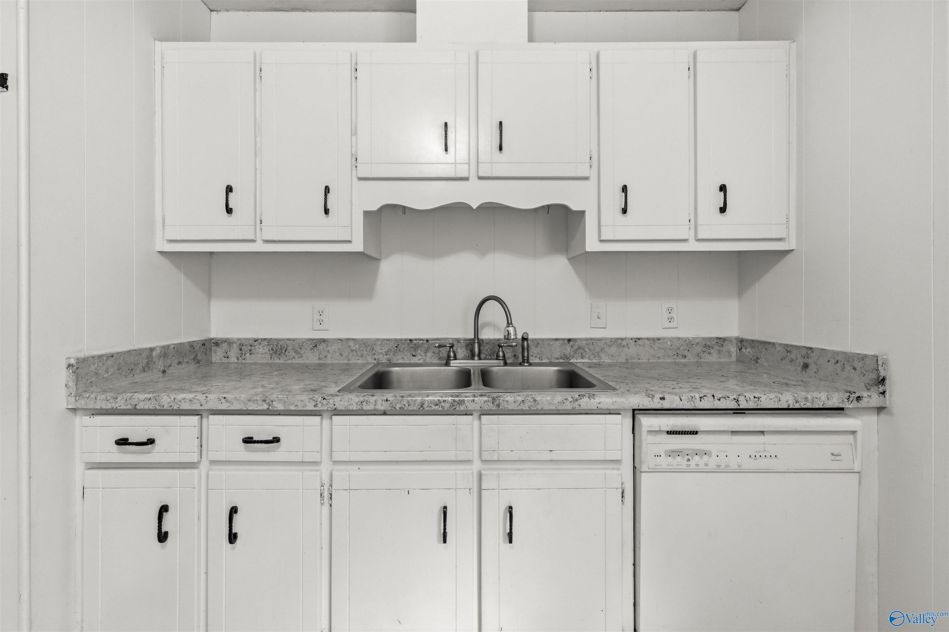 Kitchen with white cabinets, a double-basin sink, mottled countertops, and a built-in dishwasher.