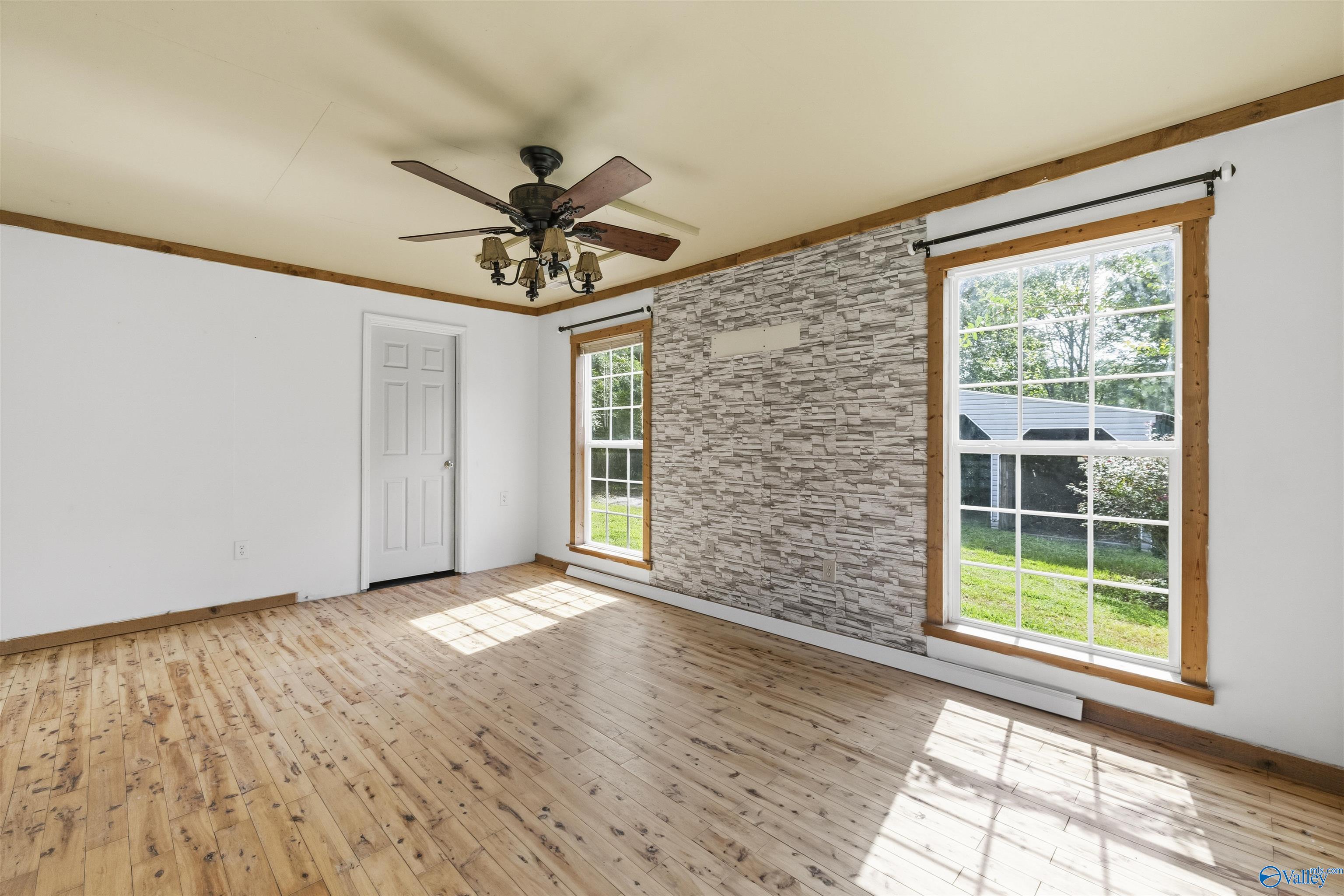 Empty living room with wood floors, a stone accent wall, and two large windows.