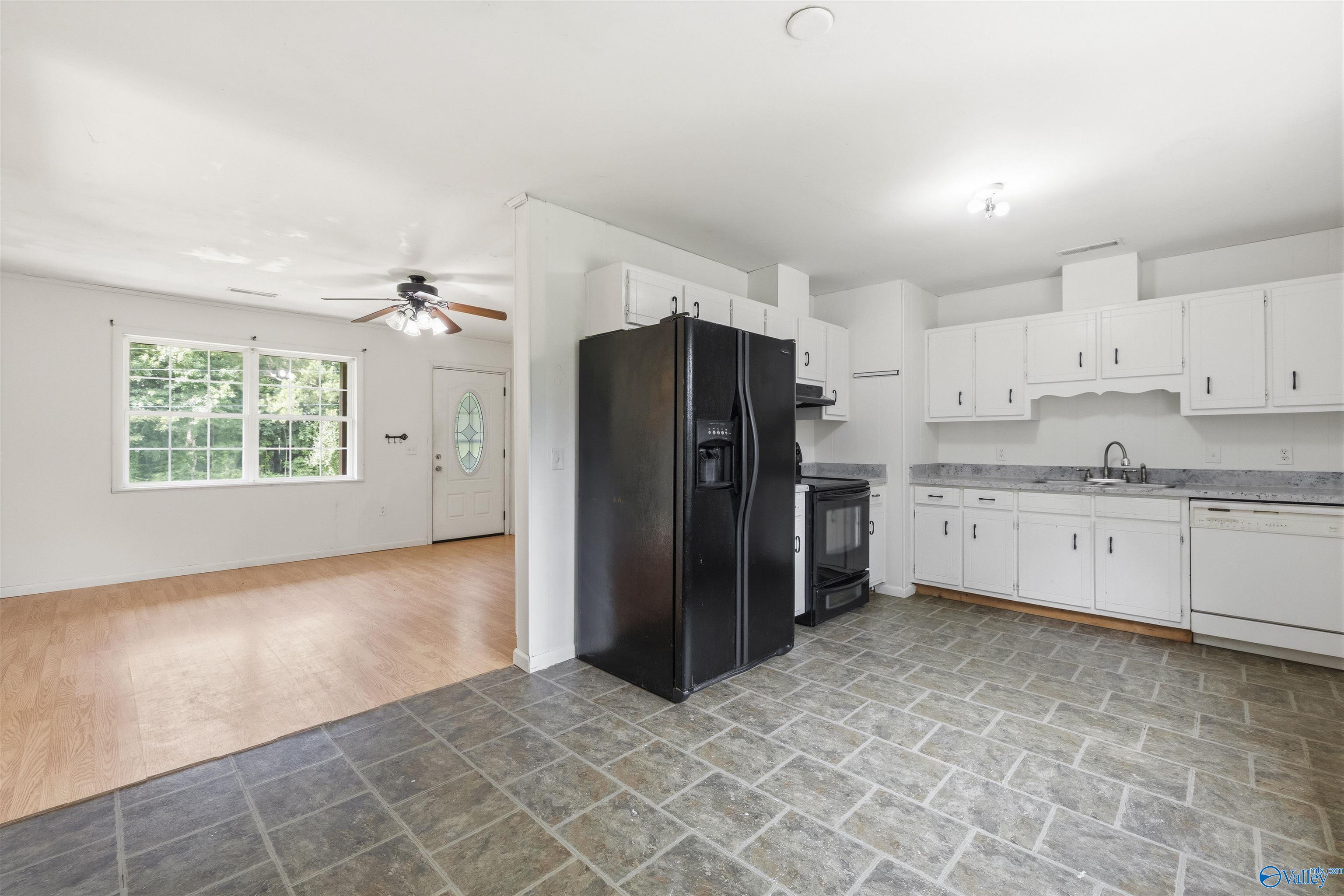 Kitchen with white cabinets and gray tile flooring, opening to a bright room with a large window.