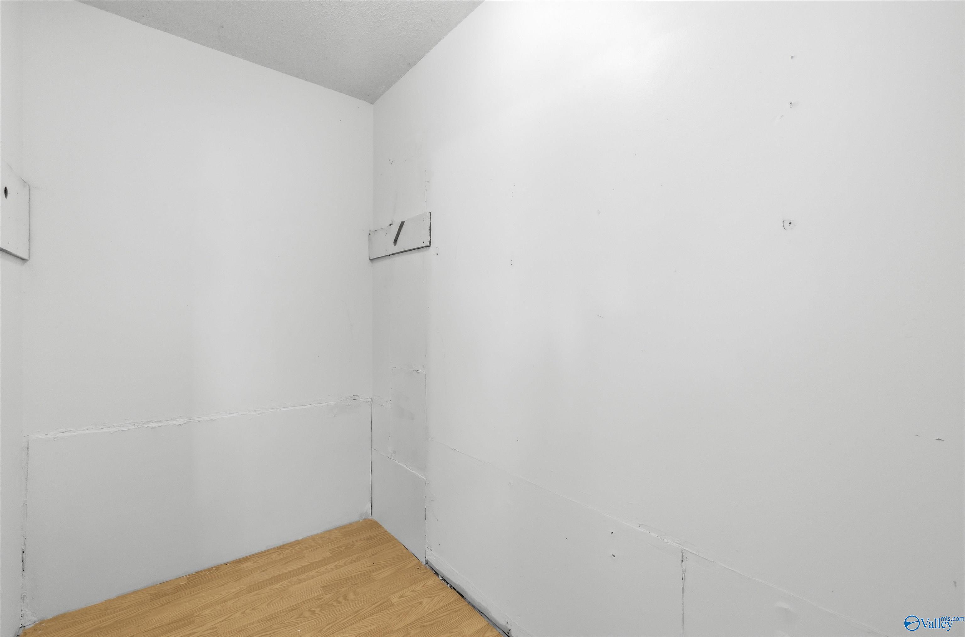 Small empty room with white walls, visible wall patches, and light wood-look flooring.