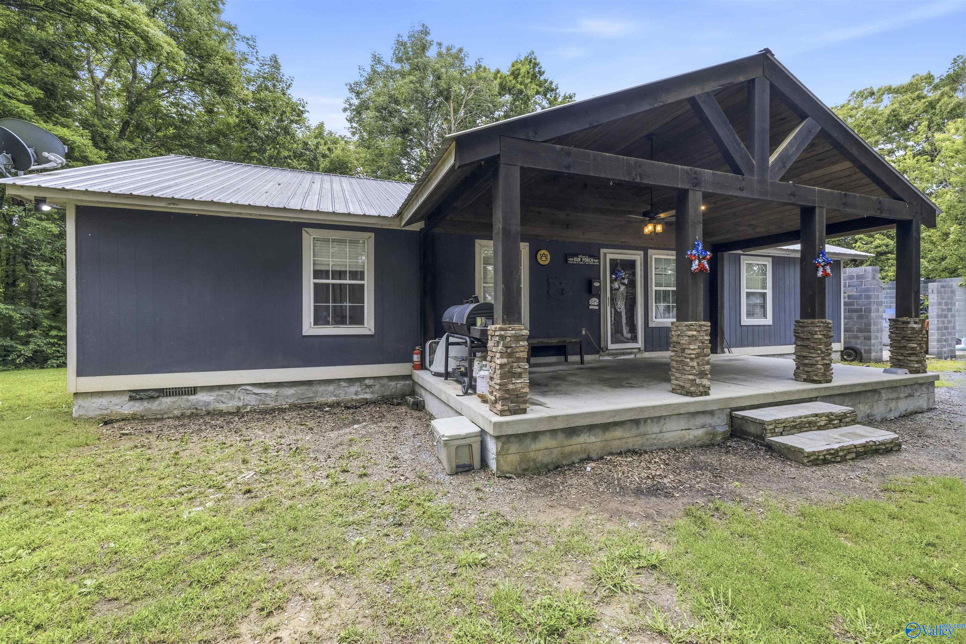 Dark blue home with a large covered porch, timber gable, stone columns, and metal roof.
