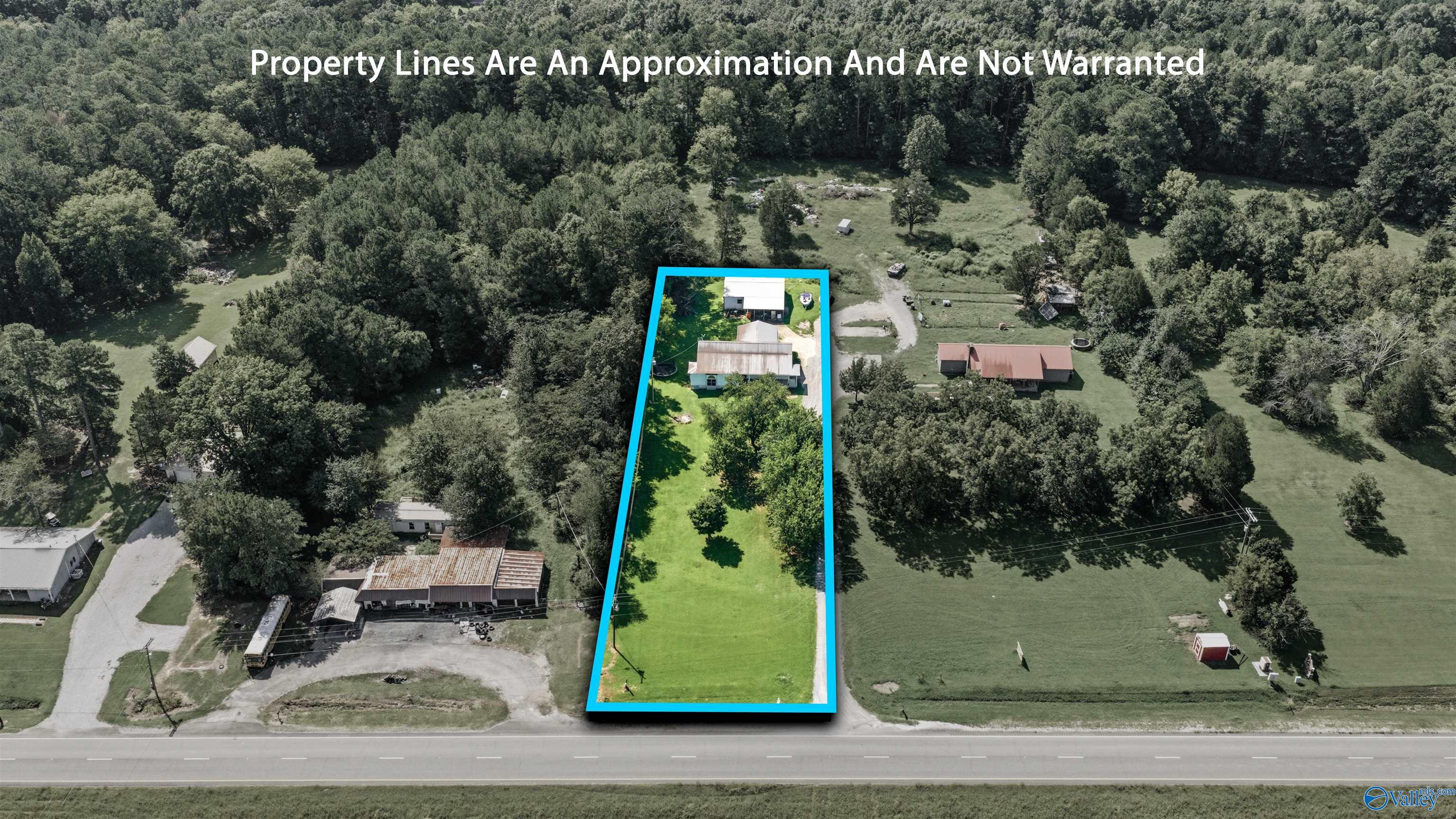 Aerial view of a long, tree-lined property outlined in blue, with a house near the back and road frontage.