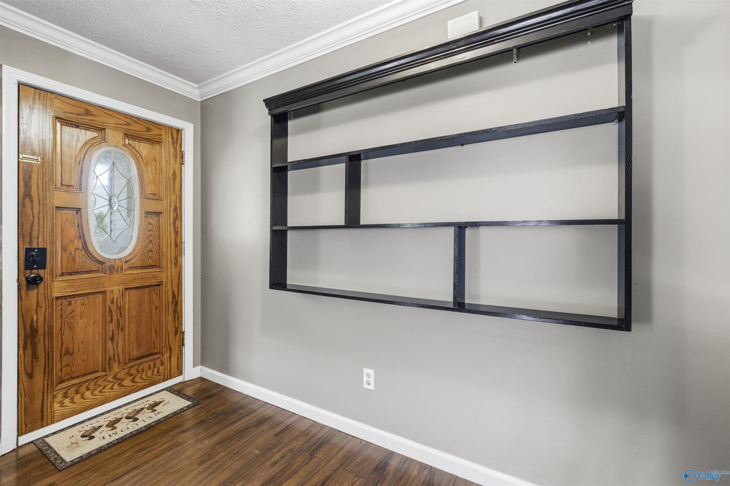 Entryway with a wooden front door featuring oval glass and large black wall-mounted shelves.
