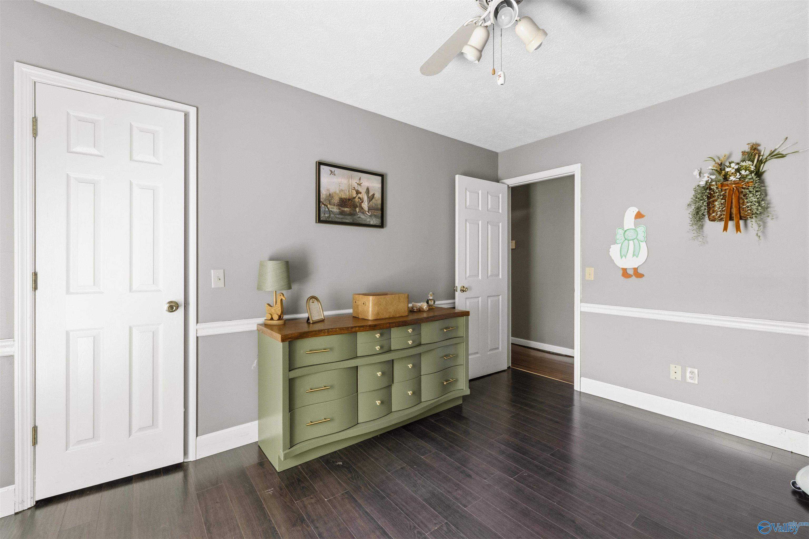Bedroom with gray walls, dark wood floors, and a sage-green dresser.