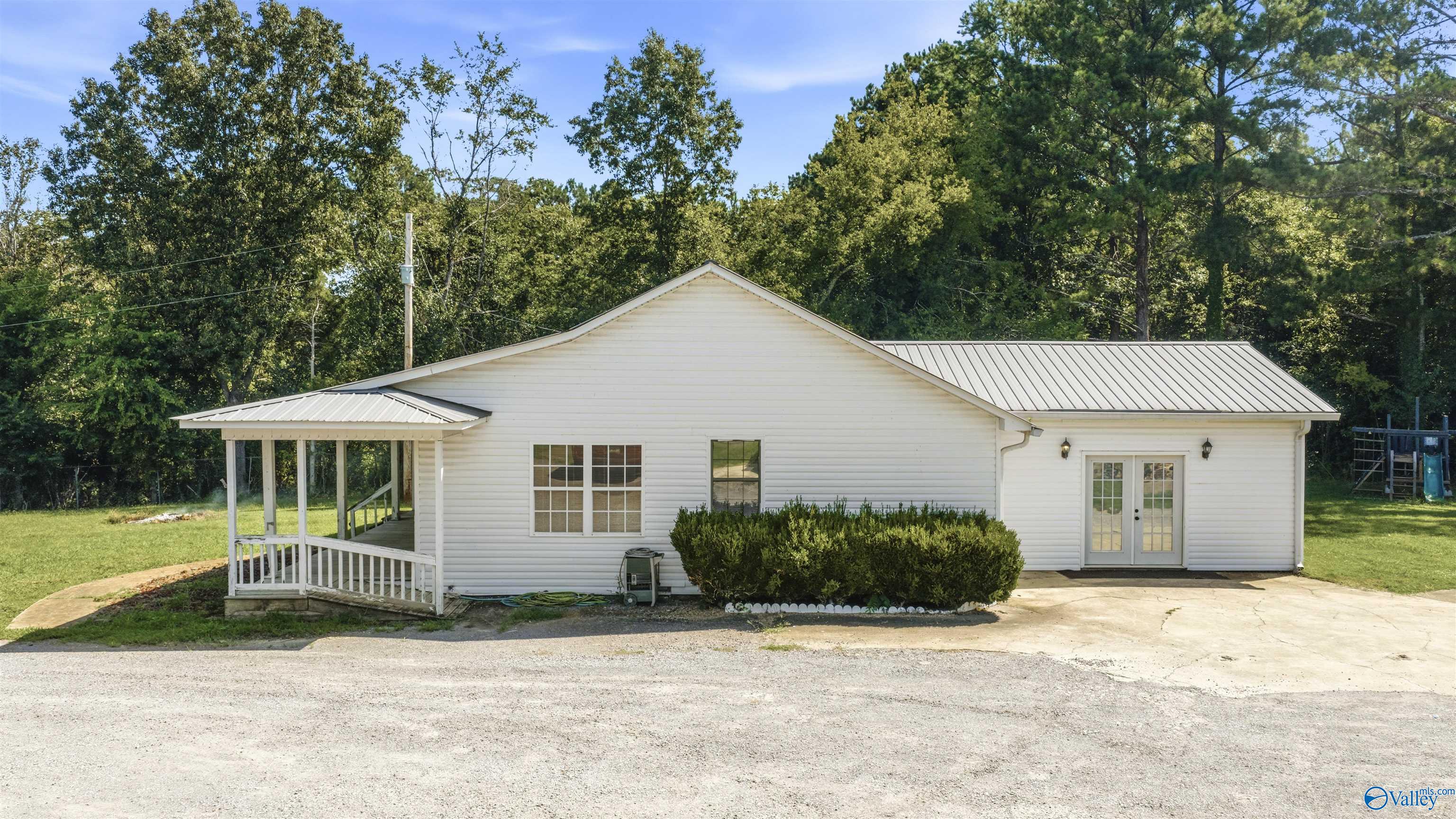 White single-story home with a metal roof, covered porch, and French doors, backed by trees.