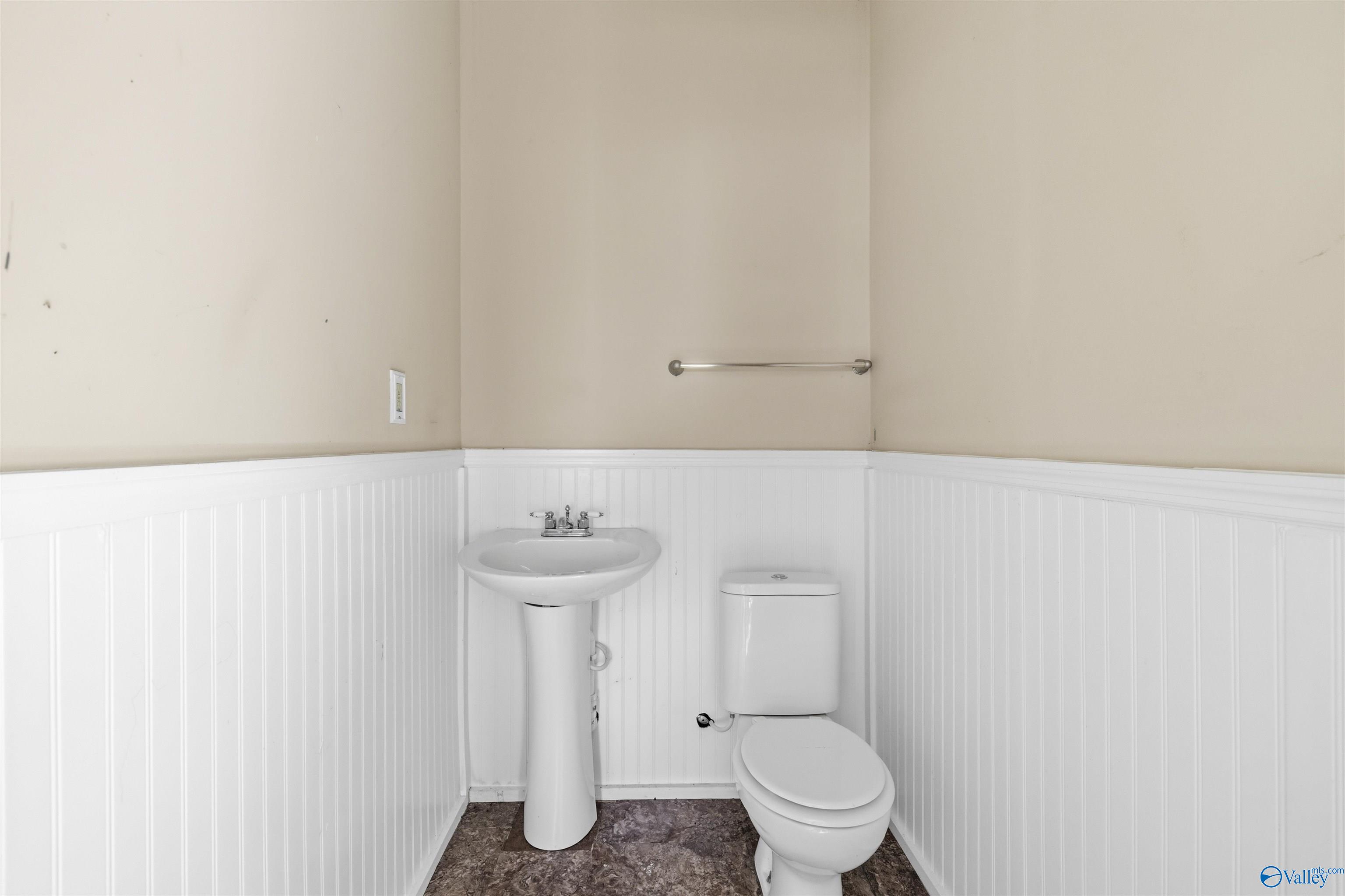Bathroom with a pedestal sink, toilet, and white beadboard wainscoting.