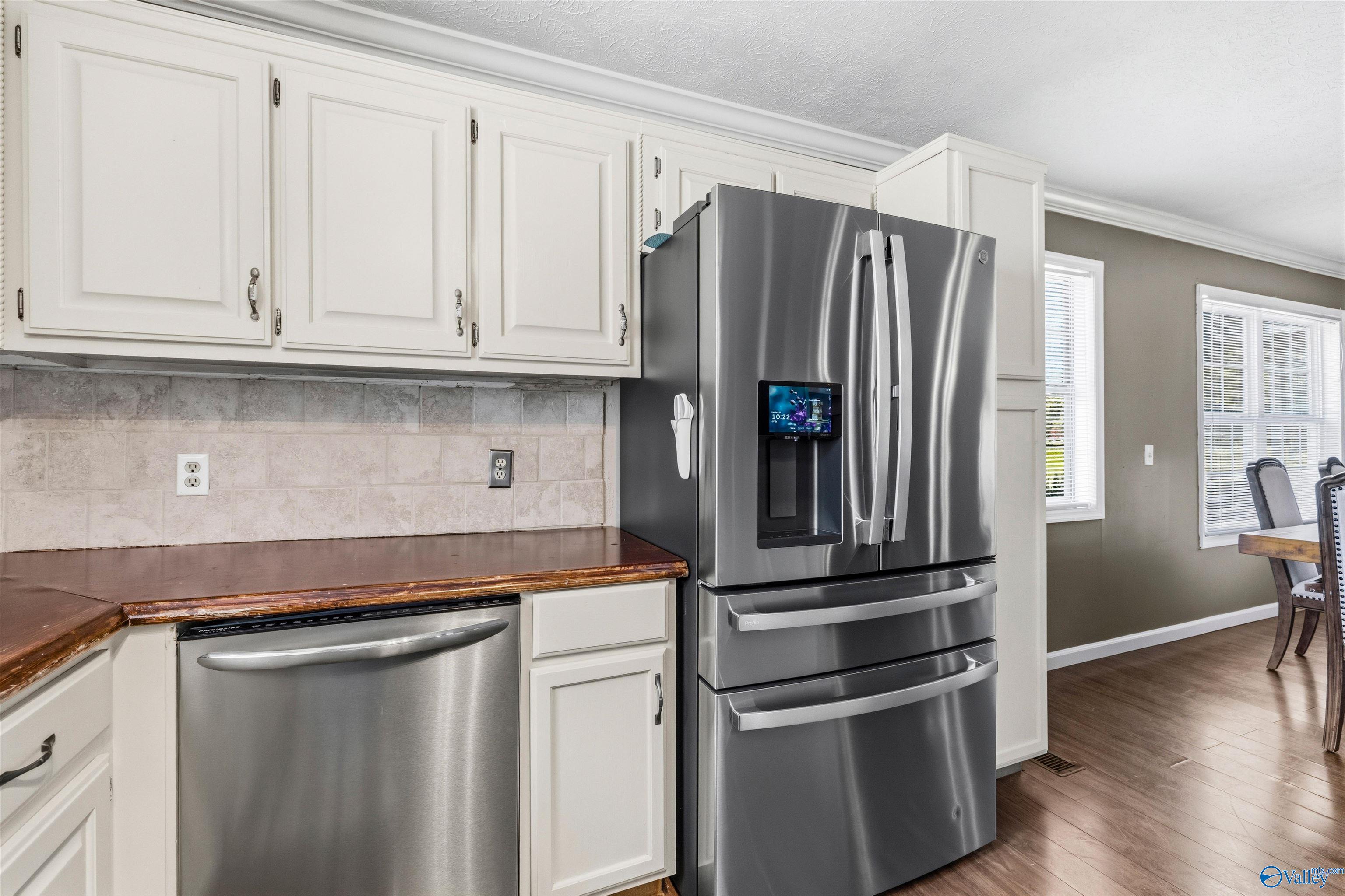 Kitchen with white cabinets, brown counters, and stainless-steel appliances, including a large refrigerator with a built-in screen.