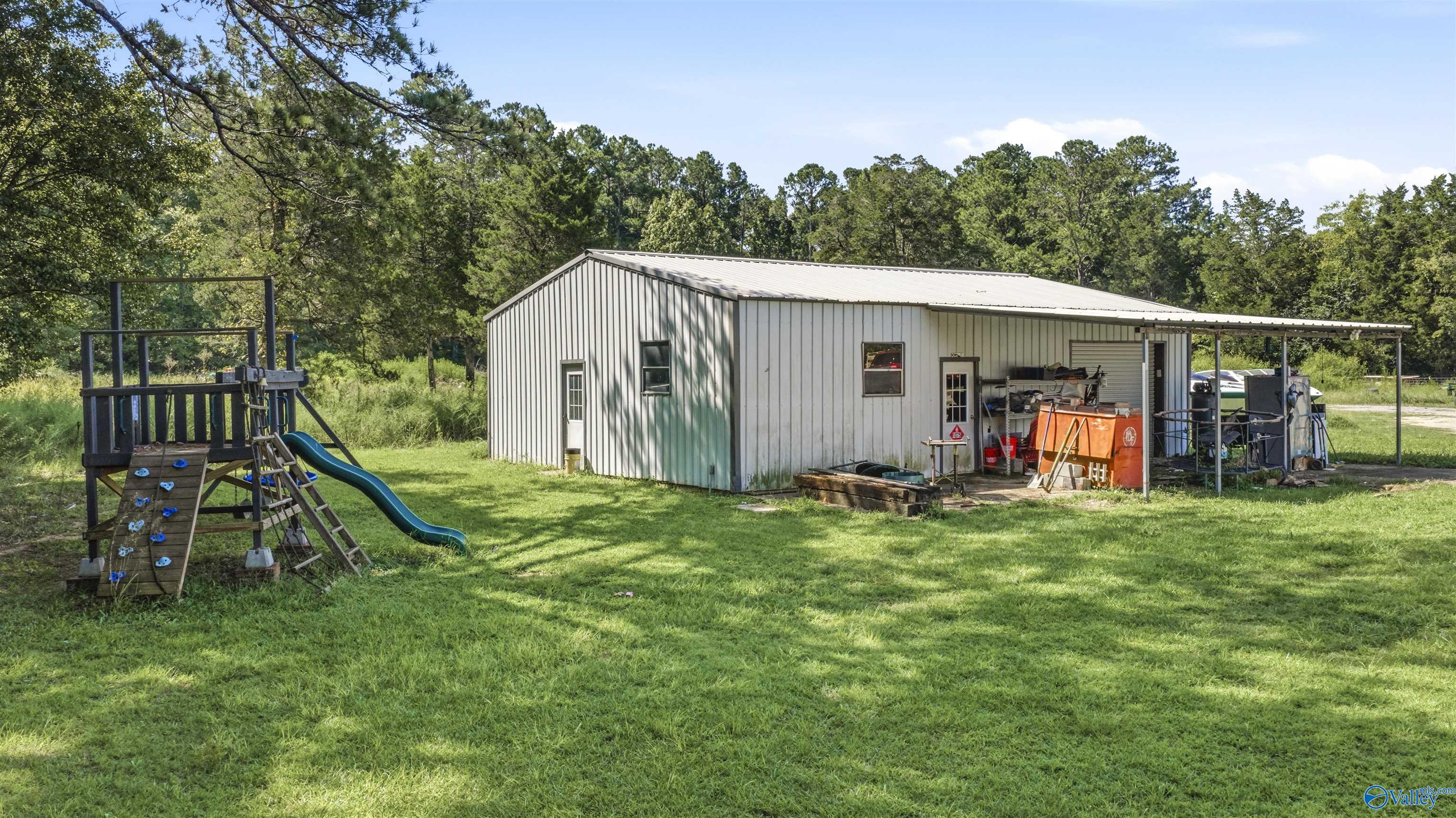 White metal workshop with covered work area beside a wooden playset and blue slide.