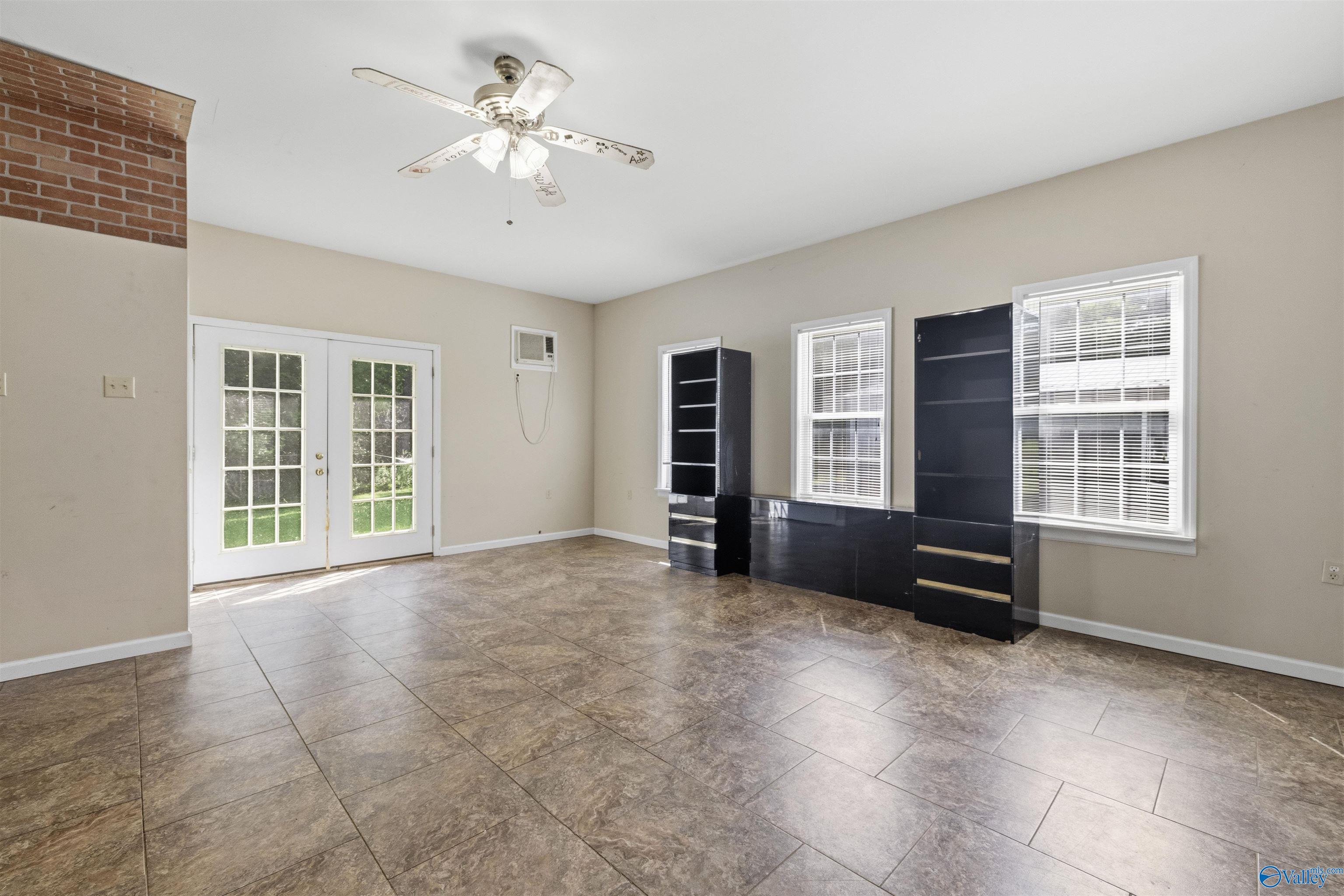 Mostly vacant room with large tile flooring, French doors, and black shelving beneath three windows.