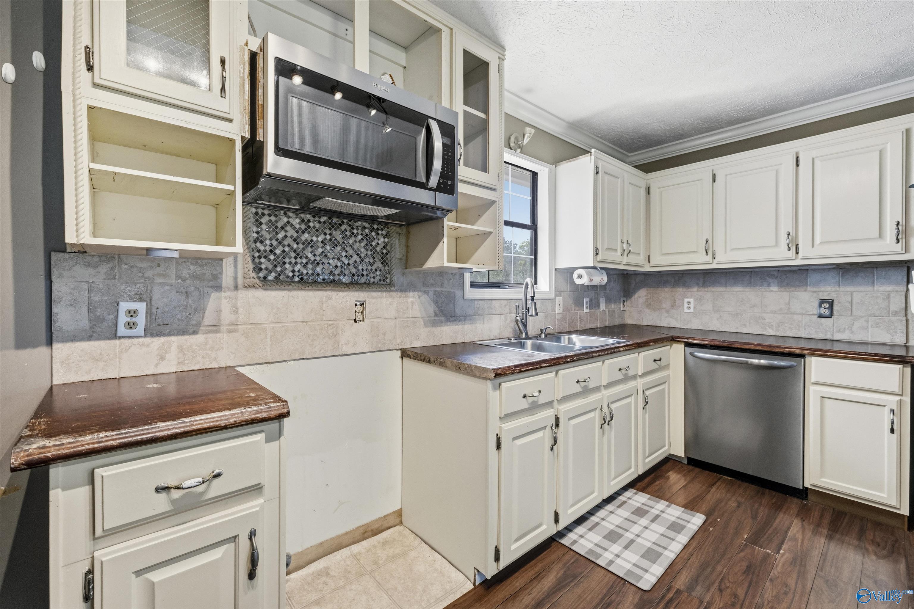 Kitchen with white cabinets, open shelving, stainless steel appliances, and a sink beneath the window.