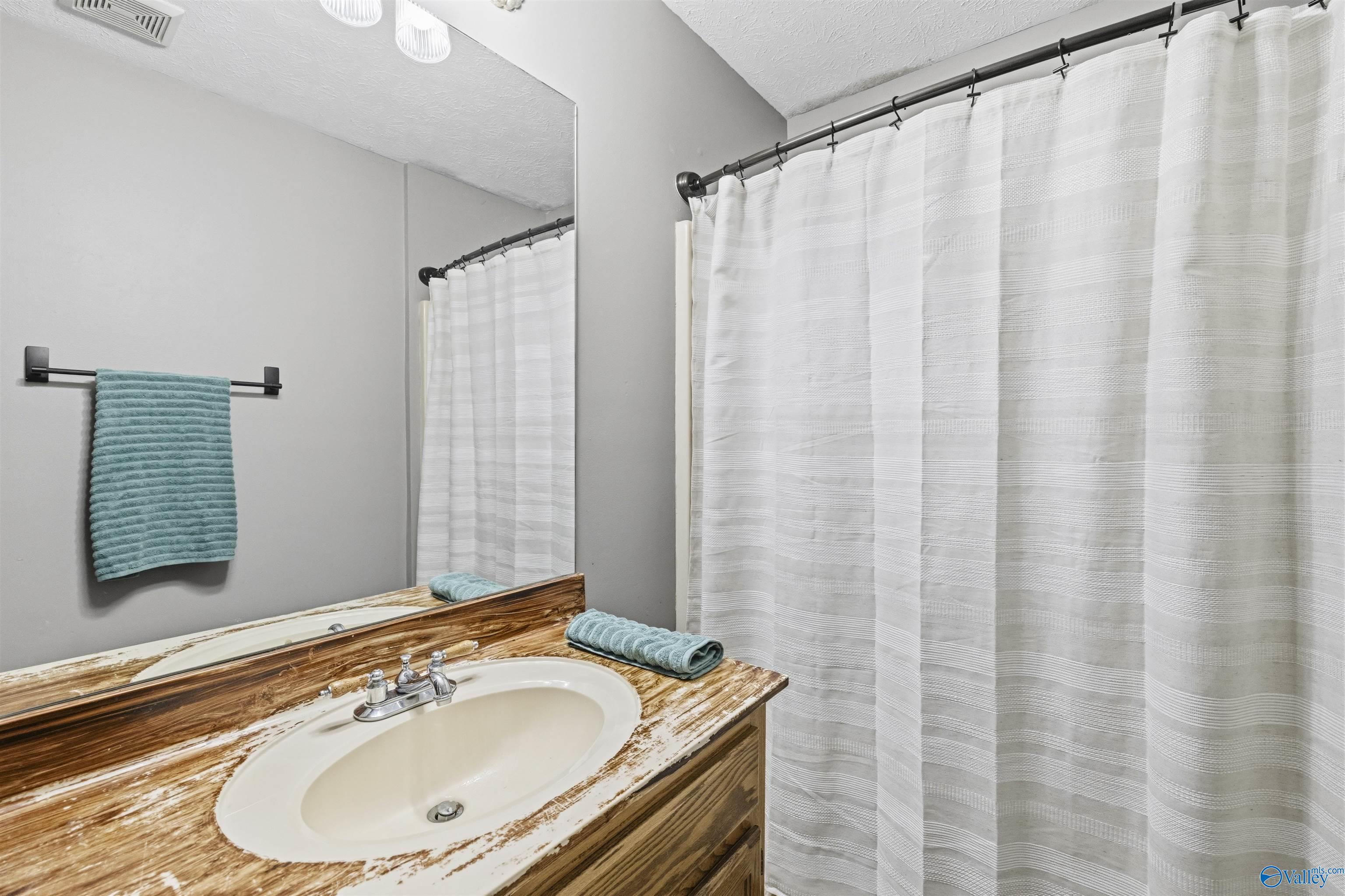 Bathroom vanity with a distressed wood counter, oval sink, large mirror, and striped shower curtain.