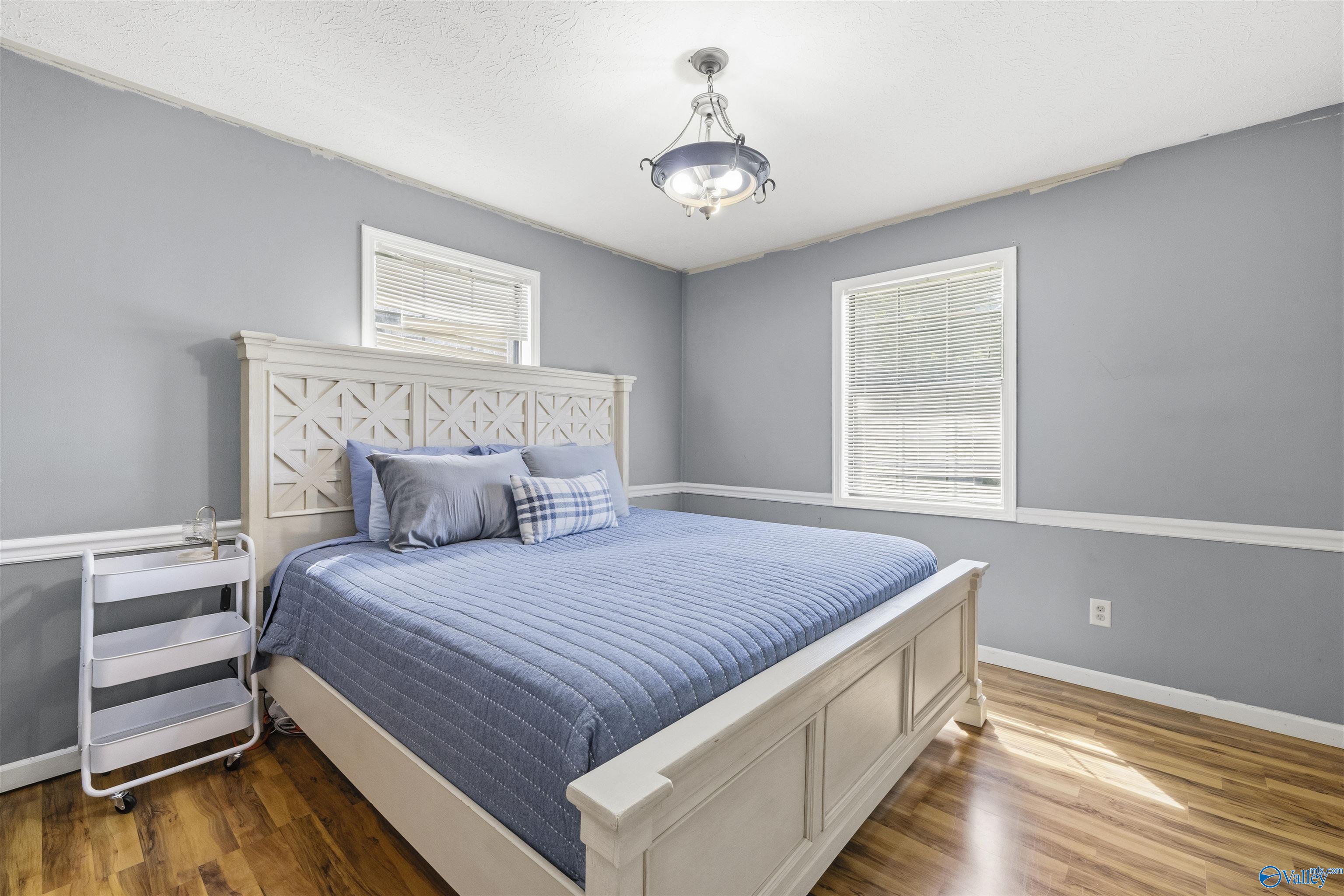 Bedroom with a large white paneled bed, blue bedding, gray walls, and hardwood floors.